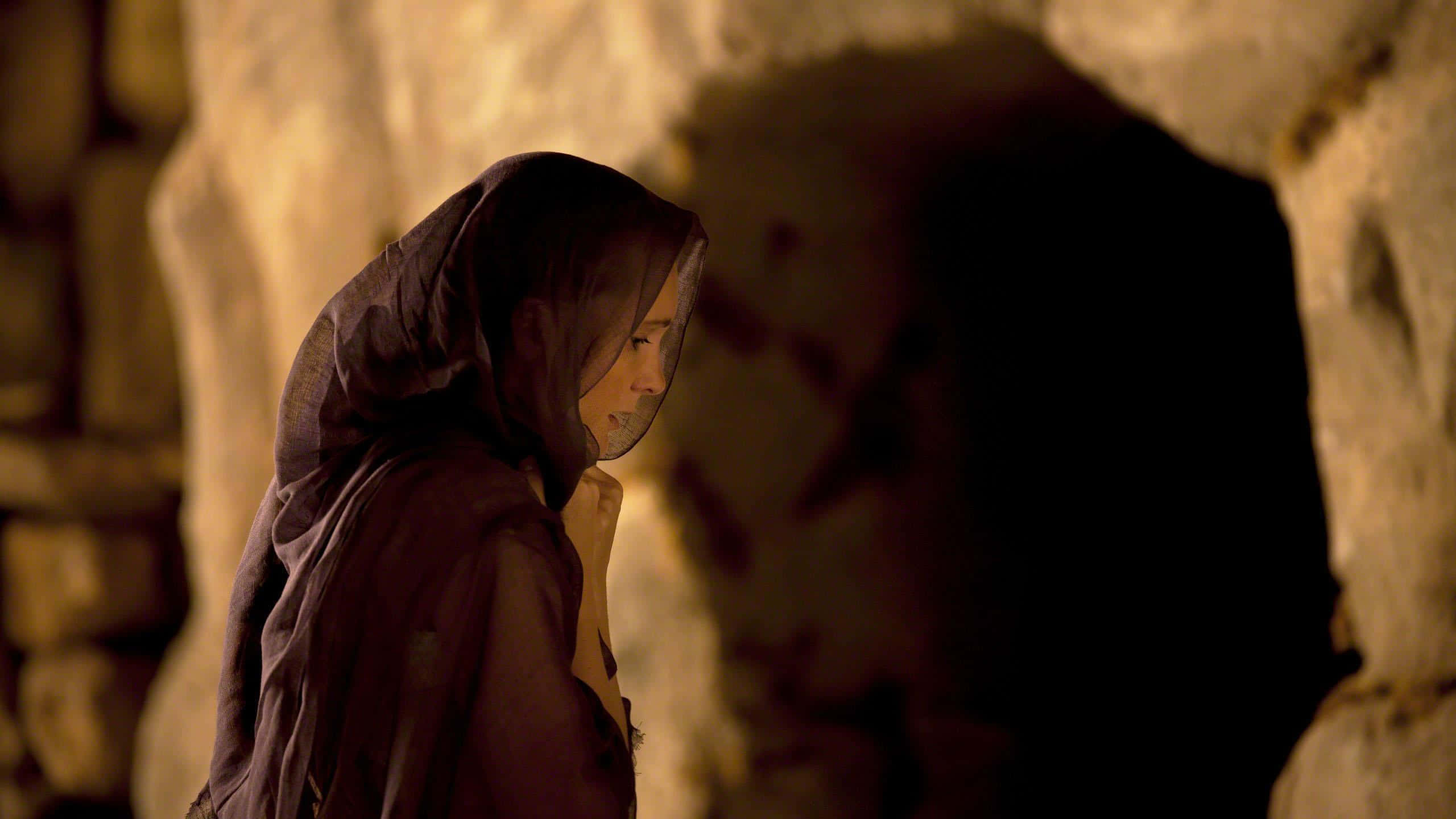 Mary Magdalene 桌布 壁紙 — 一位戴著深色面紗的女子站在光線昏暗的石洞中，她的臉龐部分被溫暖的光線照亮。