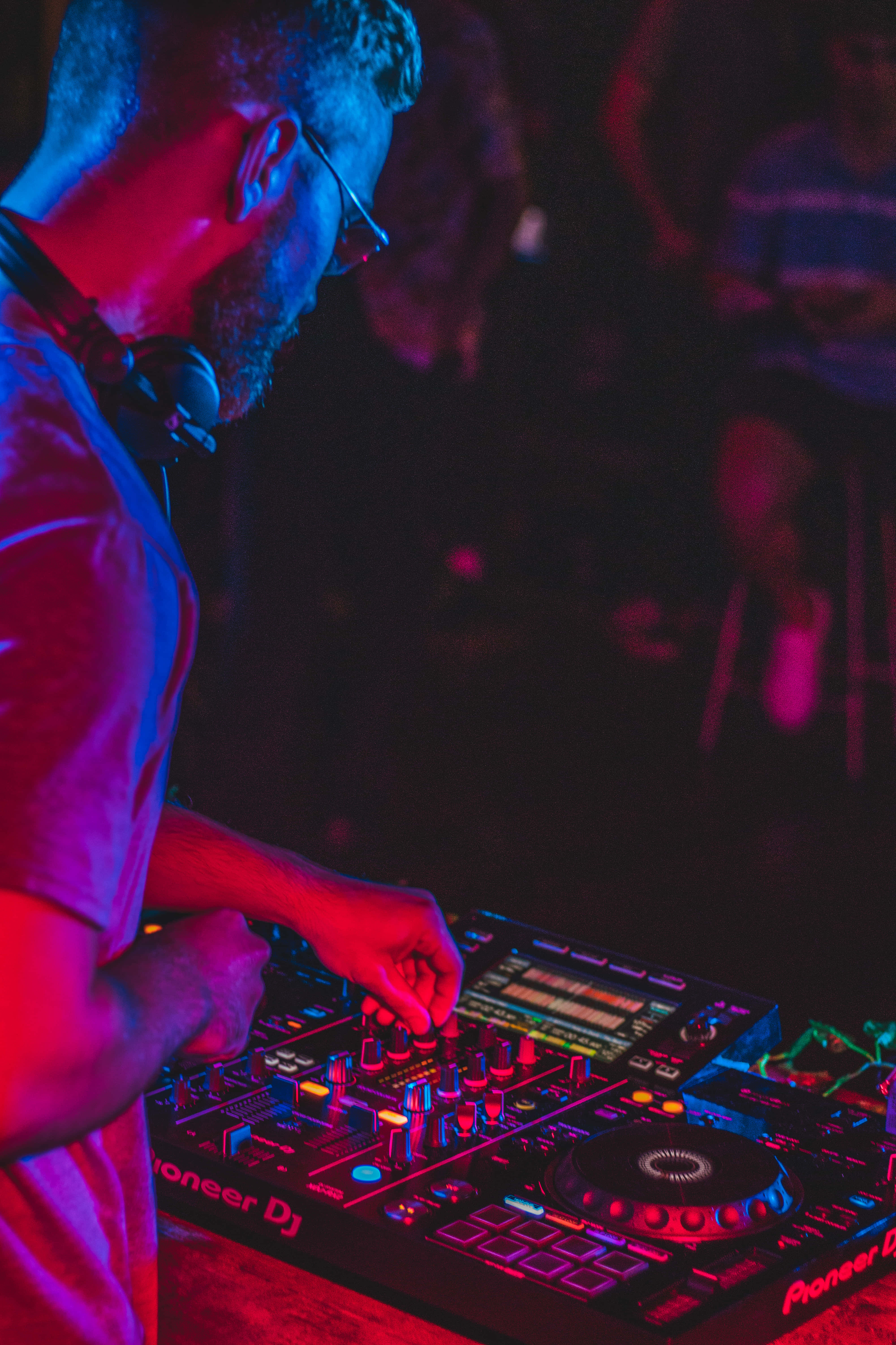 DJ 桌布 壁紙 — 一位戴著眼鏡和耳機的DJ在充滿活力的紅色和藍色俱樂部燈光下，使用Pioneer DJ控制器混音音樂。