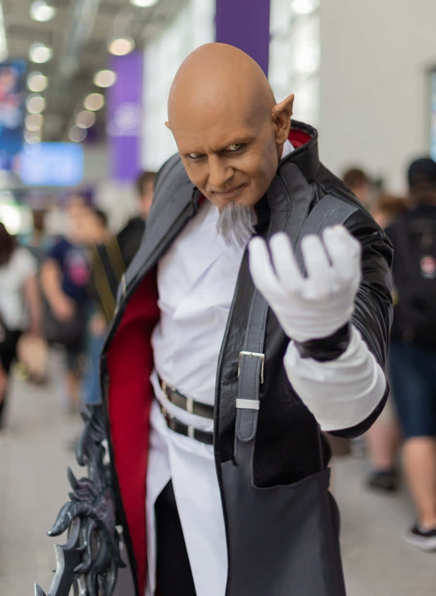 Kingdom Hearts Xehanort 桌布 壁紙 — 一位戴著精靈耳朵和山羊鬍子的角色扮演者在會議廳中擺出戲劇性的姿勢，身穿黑色外套、紅色襯裡和白色手套。