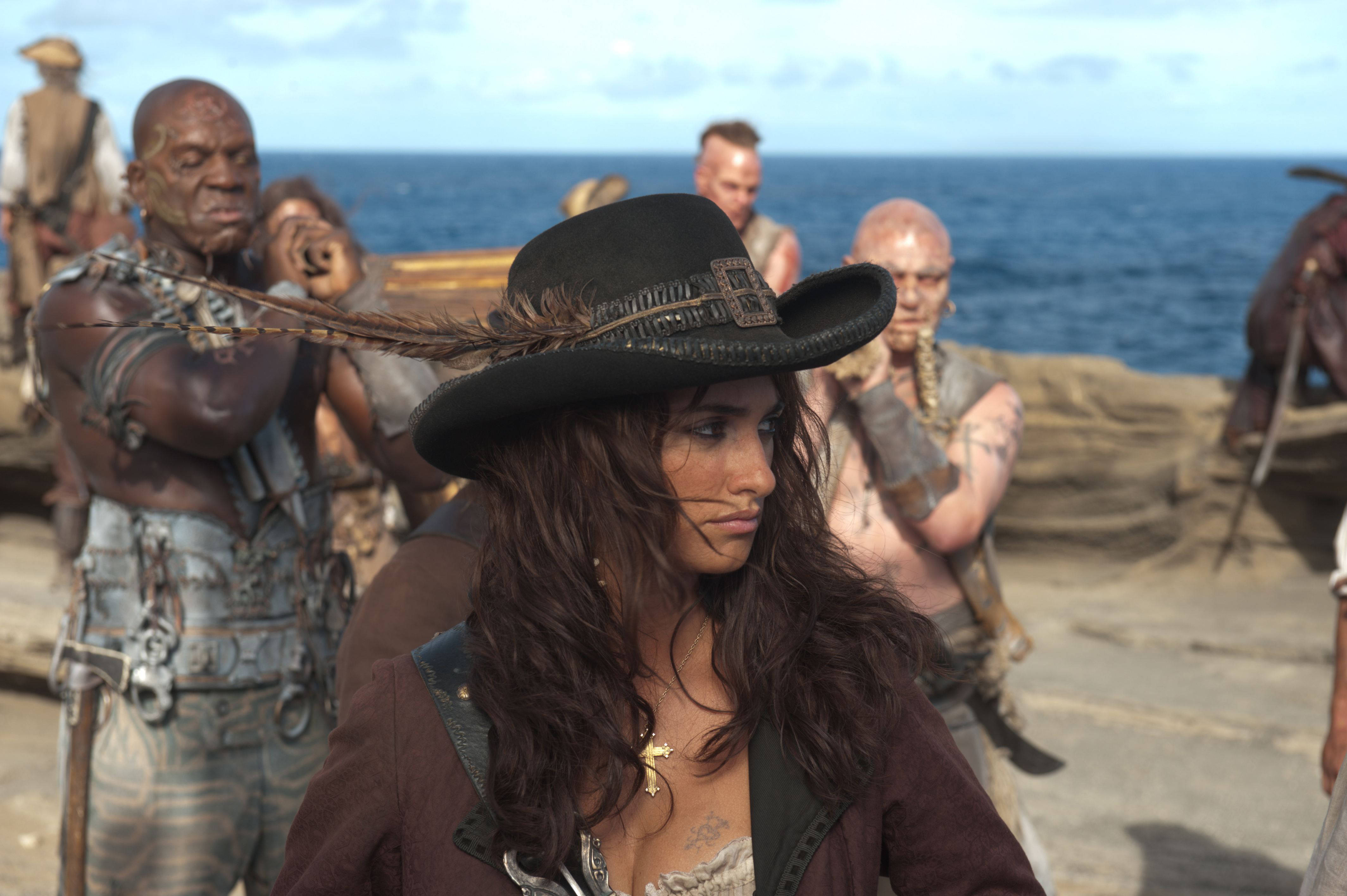 Pirates Of The Caribbean 桌布 壁紙 — 一位戴著羽毛帽的兇猛女海盜站在船甲板上，與紋身船員一起，背景是廣闊的海洋。