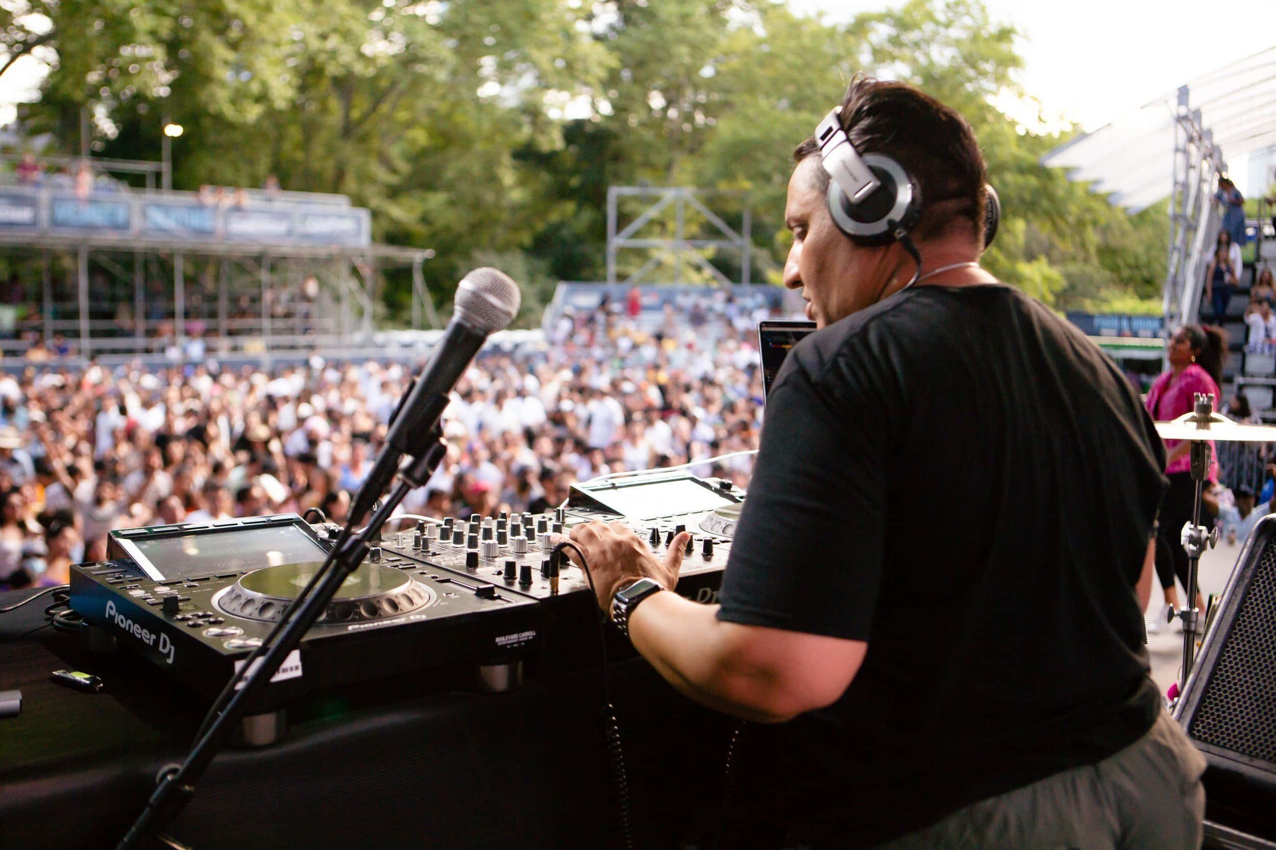 DJ 桌布 壁紙 — 一位戴著耳機的DJ在戶外音樂節上混音，身後擠滿了歡呼的人群。