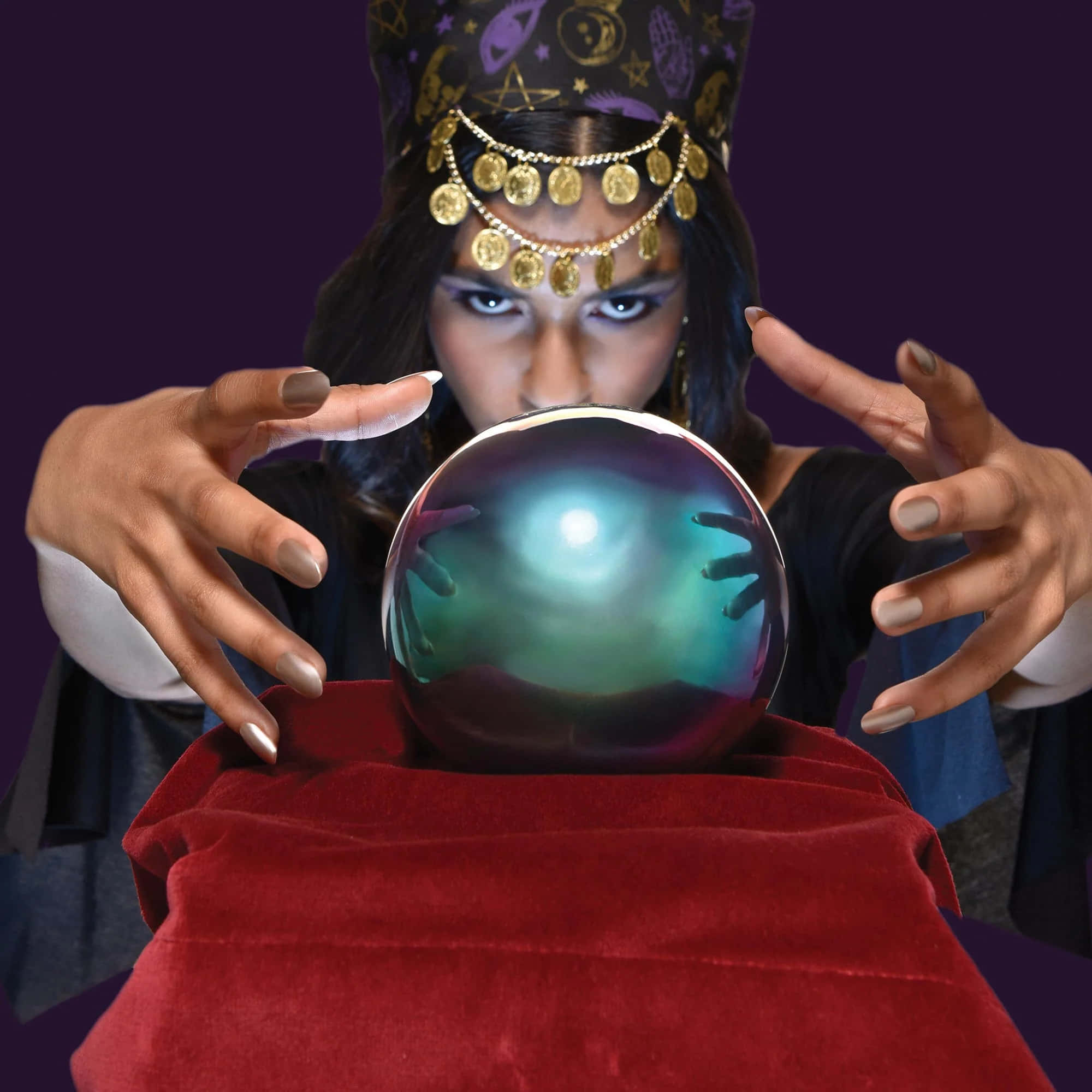 Fortune Teller 桌布 壁紙 — 一位戴著金幣和星星頭飾的神秘主義者，透過放在紅色天鵝絨上的發光水晶球凝視著。