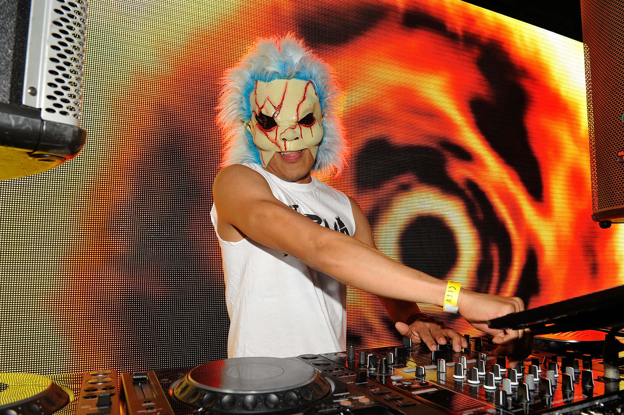 DJ 桌布 壁紙 — 一位戴著面具、藍色頭髮的DJ在俱樂部中混音，背景是火熱的橙色和黑色LED燈光。