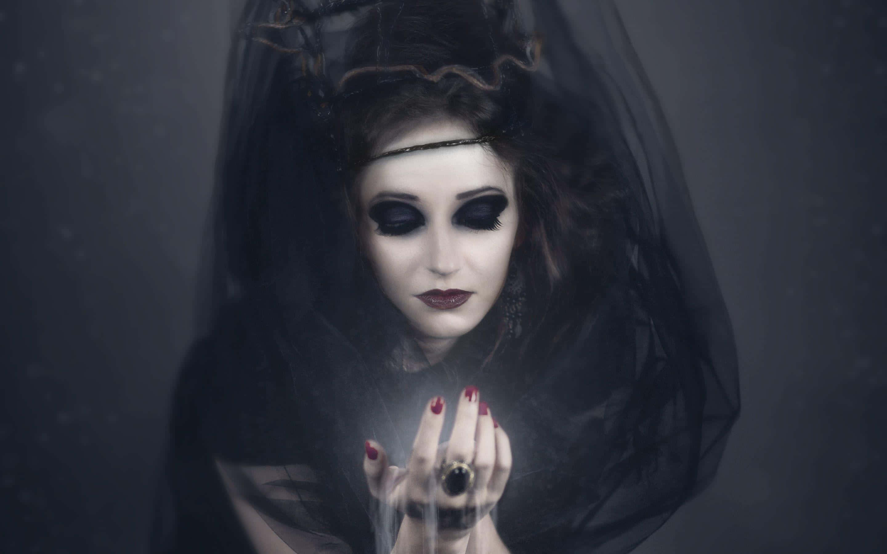 Horror Costumes 桌布 壁紙 — 一位戴著黑色面紗、妝容誇張的女性，在黑暗迷濛的背景中雙手捧著一個發光的球體。