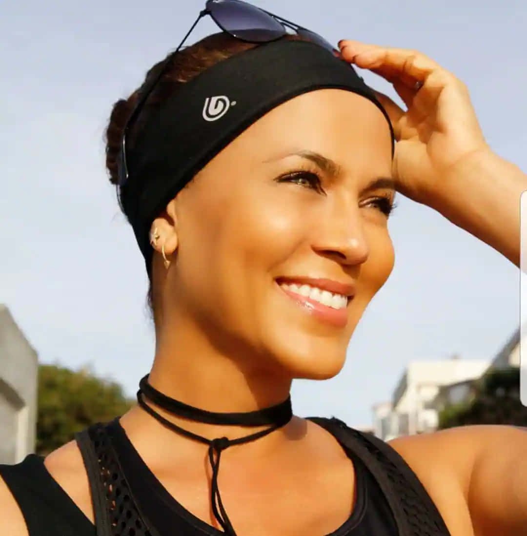 Nicole Ari Parker 桌布 壁紙 — 一位戴著黑色頭帶和背心的微笑女士在明亮的戶外背景下調整她的太陽眼鏡。