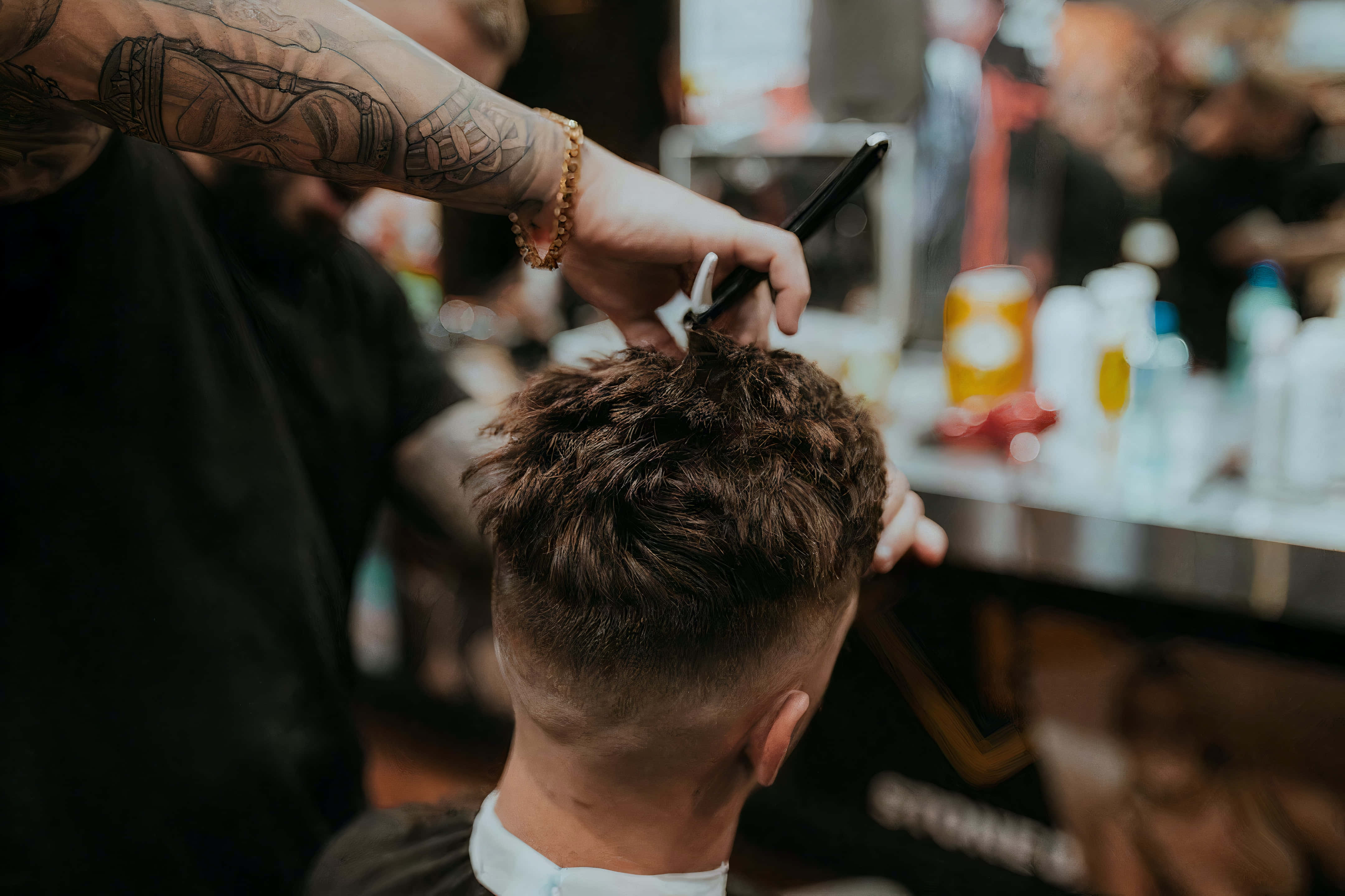 Barber 桌布 壁紙 — 一位手臂有紋身的理髮師在繁忙的理髮店裡用剪刀修剪顧客的深色頭髮。