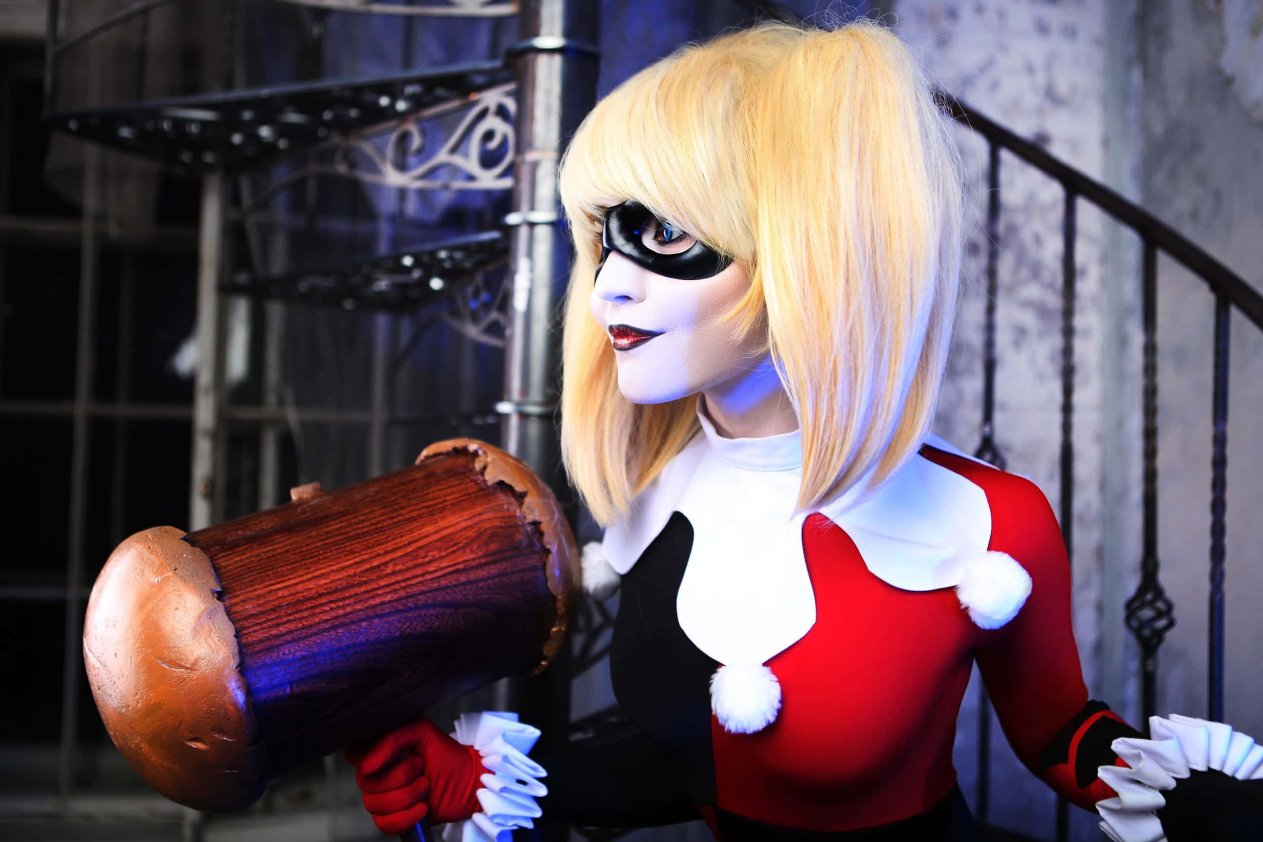 Harley Quinn Hammer 桌布 壁紙 — 一位扮演哈莉·奎茵的角色扮演者在一個光線昏暗、有金屬樓梯的工業環境中手持一個大木槌。
