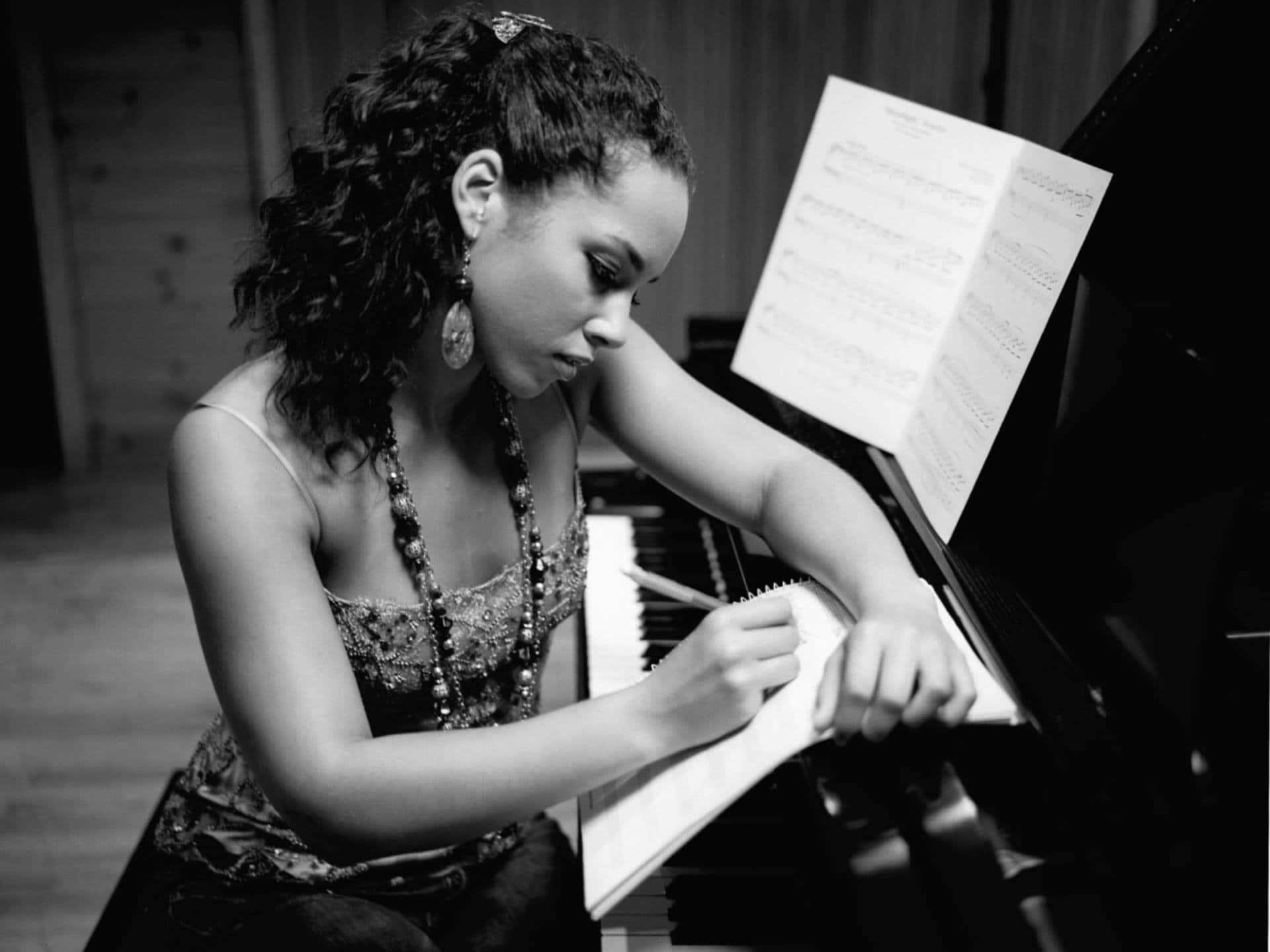 Alicia Keys 桌布 壁紙 — 一位捲髮女性在單色工作室環境中於鋼琴上書寫音符。