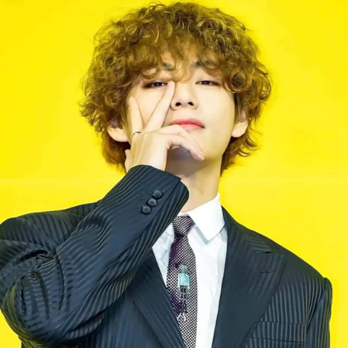 Taehyung Cute 桌布 壁紙 — 一位捲髮年輕男子穿著細條紋西裝，在亮黃色背景前將手靠近臉部擺姿勢。