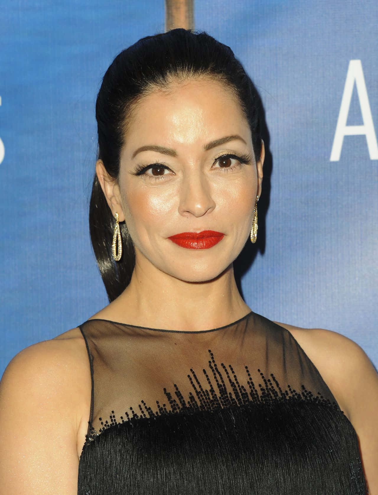 Emmanuelle Vaugier 桌布 壁紙 — 一位擁有光滑黑髮和大膽紅唇的女性，在藍色背景下穿著黑色珠飾連衣裙。