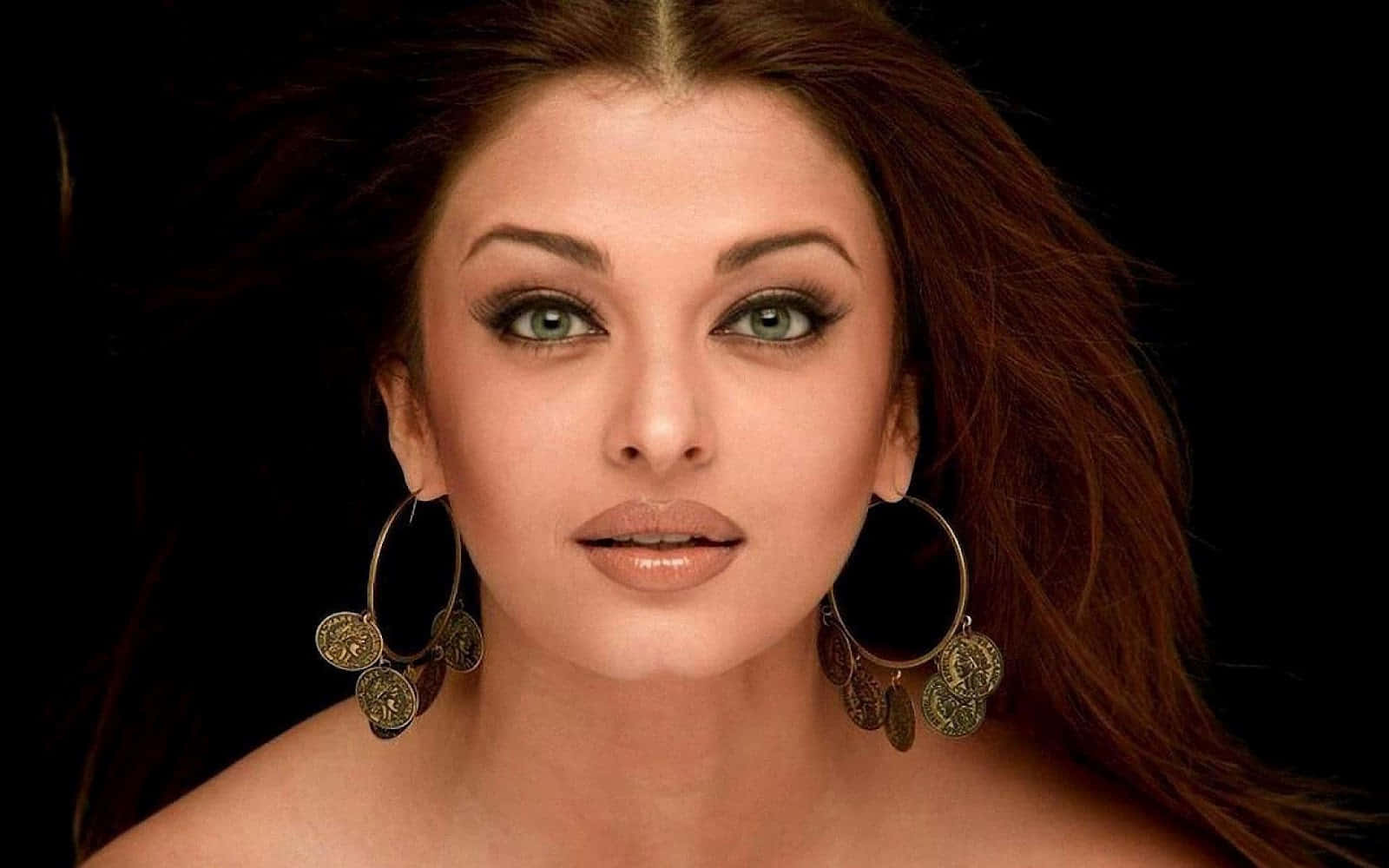 Aishwarya Rai 桌布 壁紙 — 一位擁有引人注目的綠色眼睛和大型裝飾性耳環的女性，在純黑背景下直視前方。