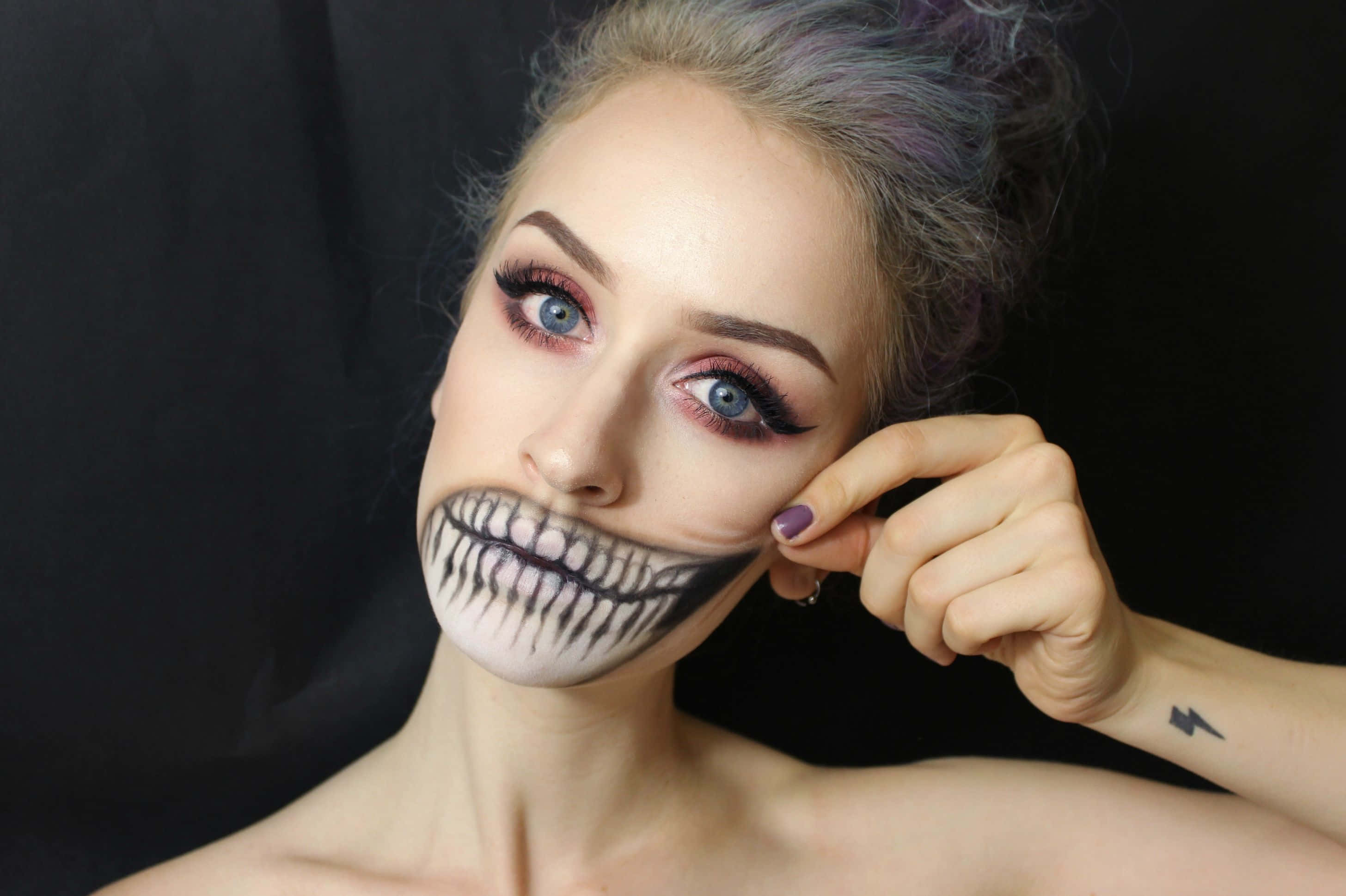 Halloween Tattoos 桌布 壁紙 — 一位擁有引人注目的藍色眼睛和紫色調頭髮的女性，在黑色背景前擺出戲劇性的骷髏妝容。