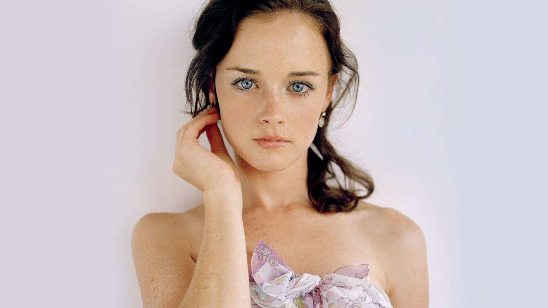 Alexis Bledel 桌布 壁紙 — 一位擁有引人注目藍眼睛和深色頭髮的女性，在純白背景上將手放在耳邊，直視鏡頭。