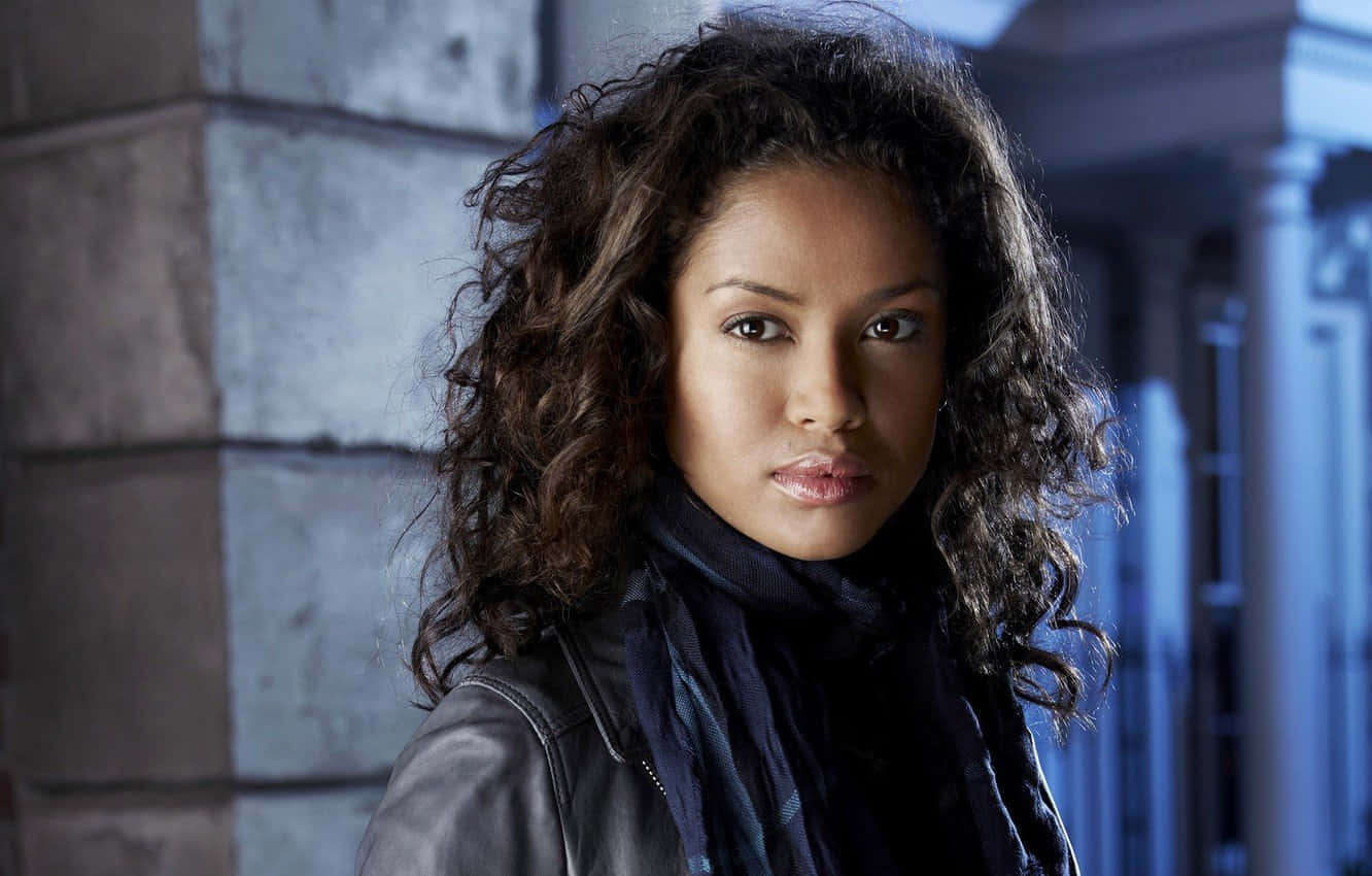 Gugu Mbatha-raw 桌布 壁紙 — 一位擁有捲曲深色頭髮、身穿皮褸的女性，在冷藍色燈光下對著石建築物凝視。