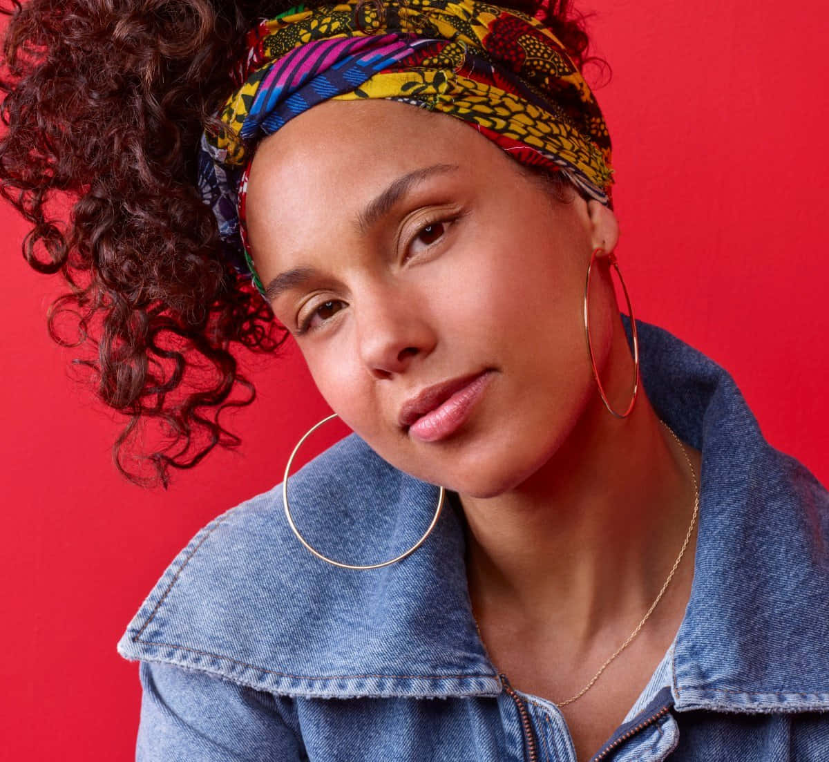 Alicia Keys 桌布 壁紙 — 一位擁有捲曲頭髮和彩色頭巾的女性，在鮮豔的紅色背景下溫柔地凝視。