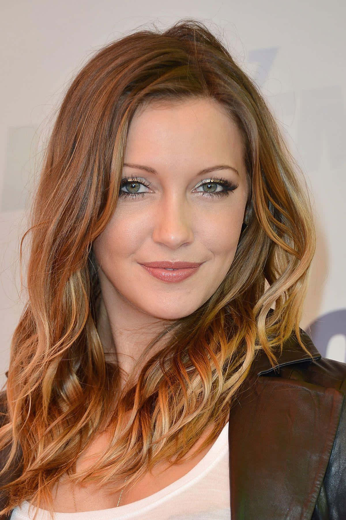 katie cassidy 桌布 壁紙 — 一位擁有波浪形赤褐色頭髮、穿著皮夾克、露出溫暖笑容的女性的特寫肖像。
