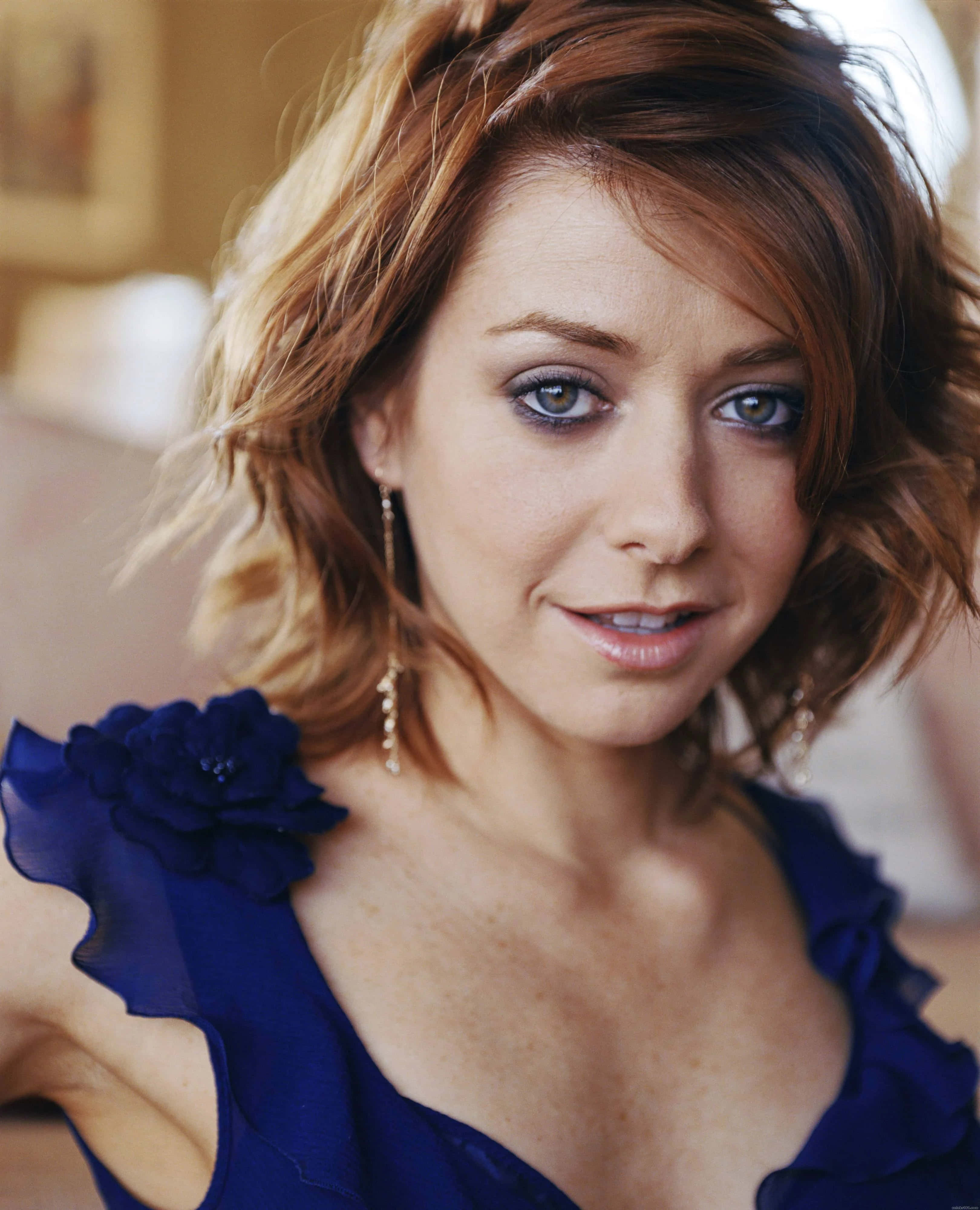 Alyson Hannigan 桌布 壁紙 — 一位擁有波浪形赤褐色頭髮和藍色眼睛的女性，穿著深藍色花卉連衣裙，溫柔地微笑。