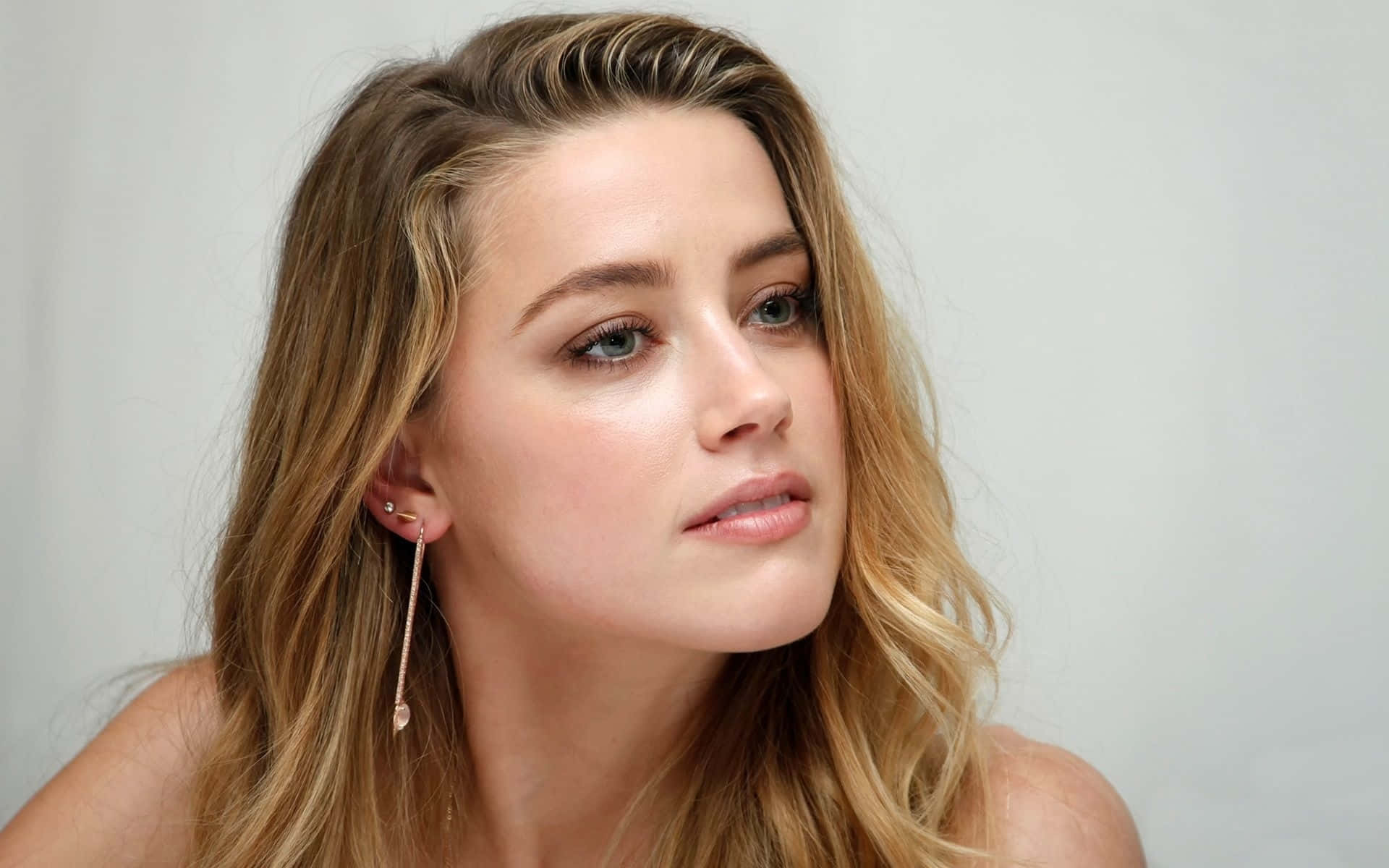 Amber Heard 桌布 壁紙 — 一位擁有波浪形金髮和玫瑰金耳環的女子的特寫肖像，背景為純白色。