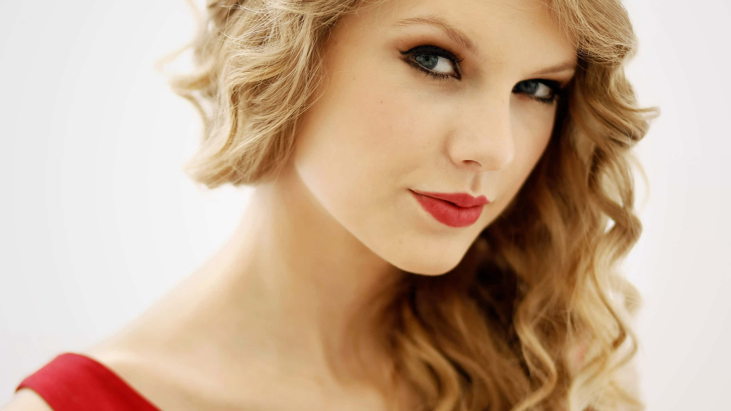 Taylor Swift 桌布 壁紙 — 一位擁有波浪形金髮和紅色唇膏的女性在柔和白色背景前的特寫肖像。