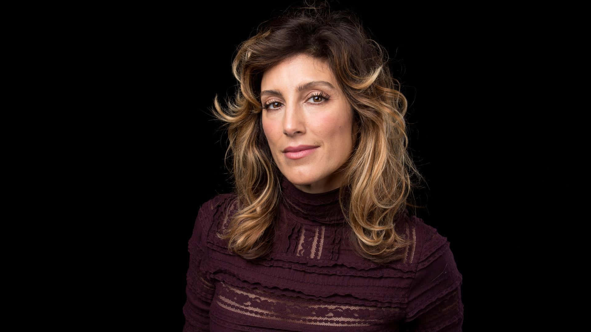 Jennifer Esposito 桌布 壁紙 — 一位擁有波浪棕色頭髮和栗色高領毛衣的女性，在黑色背景前平靜地凝視。