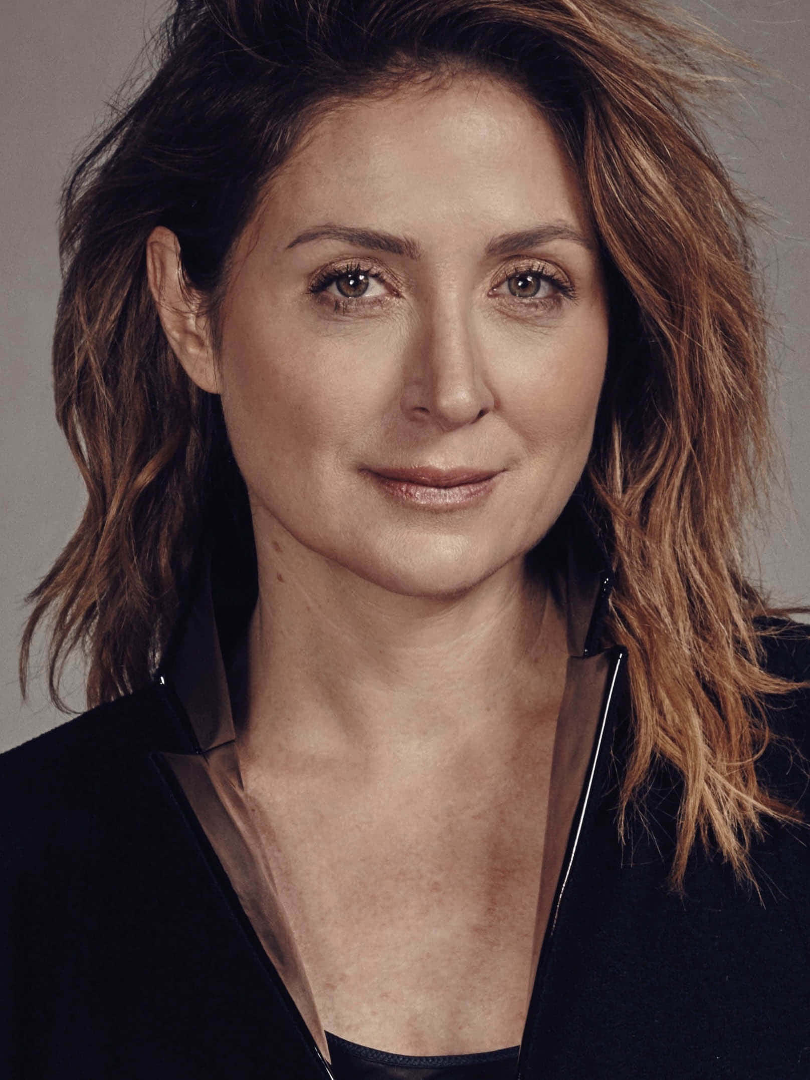 Sasha Alexander 桌布 壁紙 — 一位擁有波浪棕色頭髮和溫暖棕色眼睛的女性，穿著黑色西裝外套，在灰色中性背景前的特寫肖像。