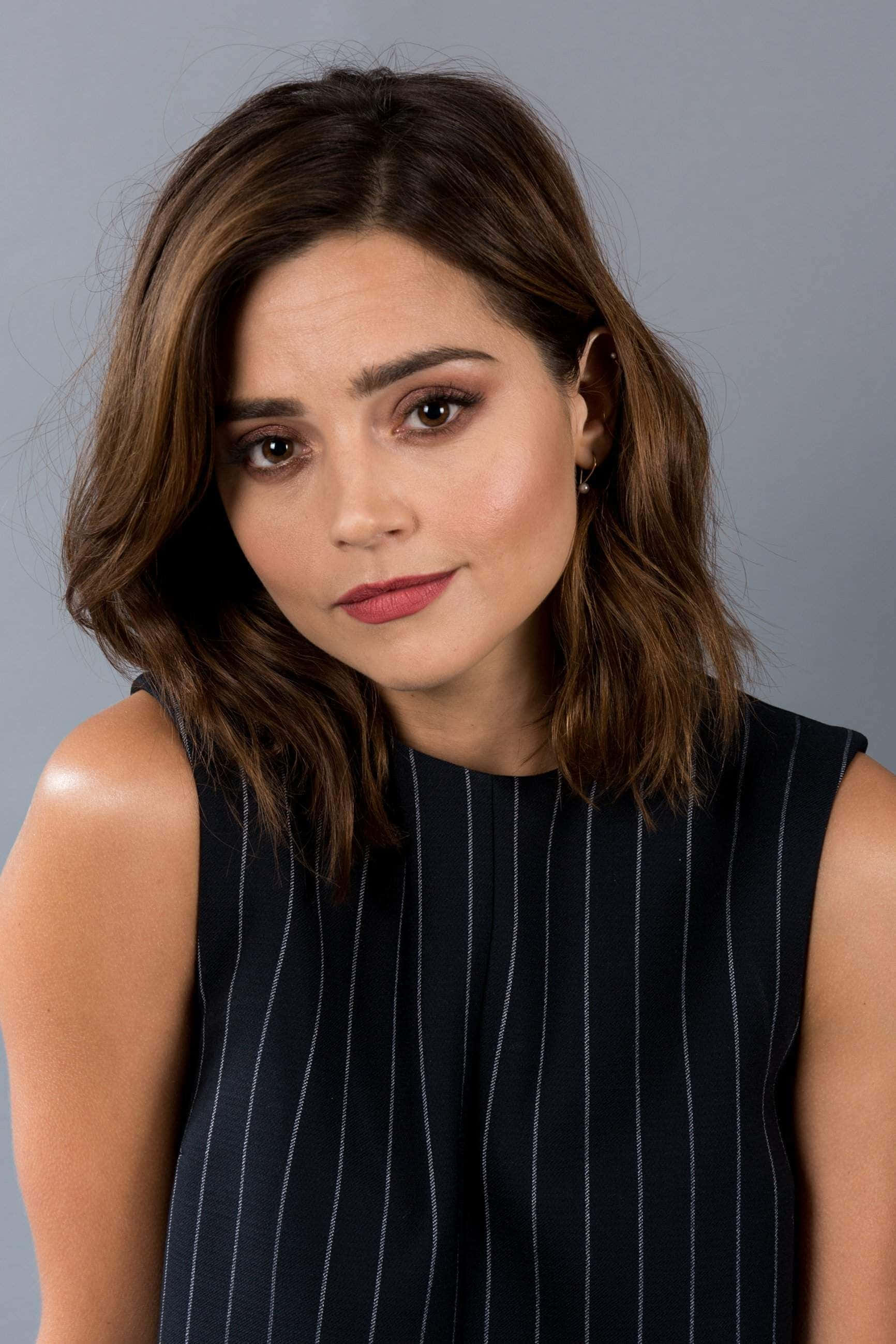 Jenna Coleman 桌布 壁紙 — 一位擁有波浪棕色頭髮和紅色唇膏的女性，在純灰色背景下溫柔地凝視著鏡頭。