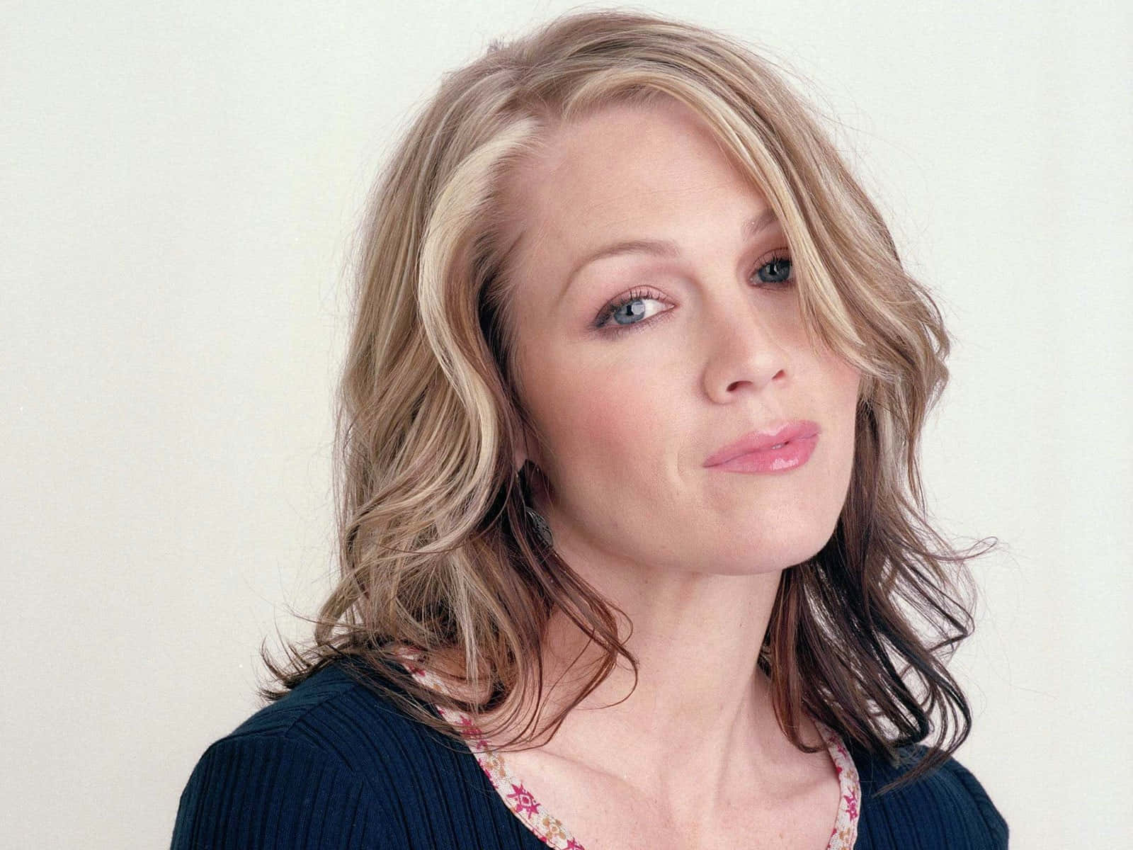 Jennie Garth 桌布 壁紙 — 一位擁有波浪金髮和藍眼睛的女性，在純白背景前溫柔凝視。