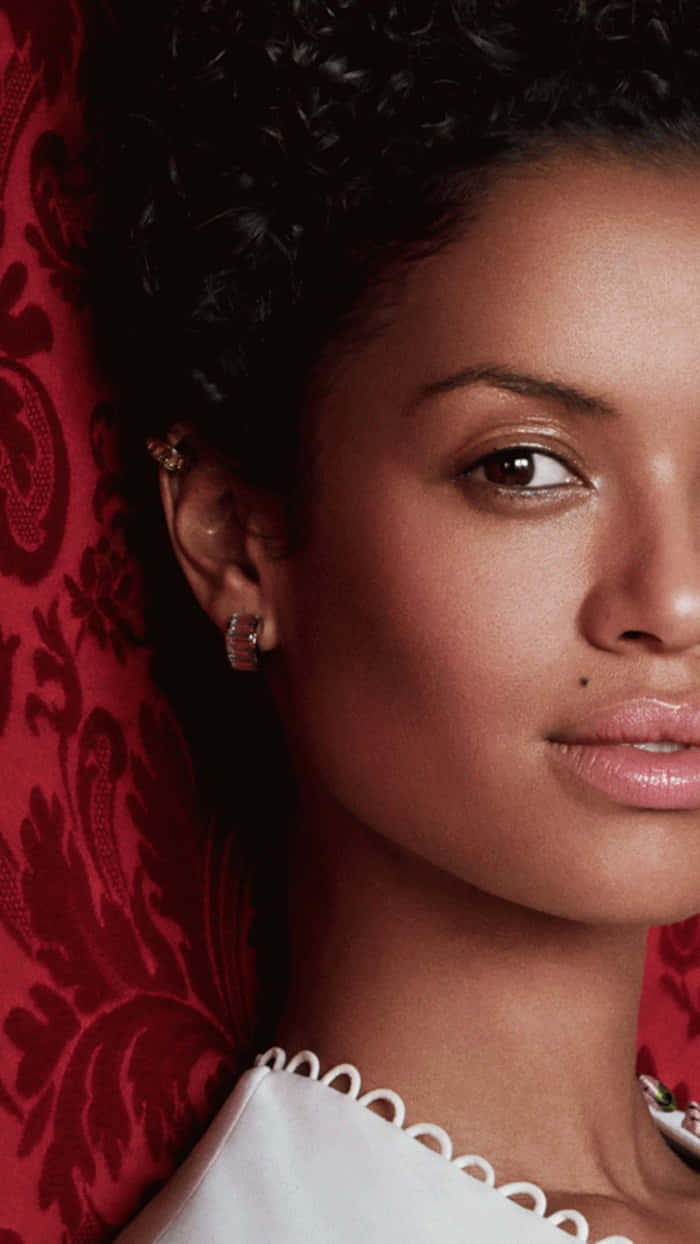 Gugu Mbatha-raw 桌布 壁紙 — 一位擁有深色捲髮和精緻珠寶的女性，以豐富的紅色錦緞布料為背景的特寫肖像。