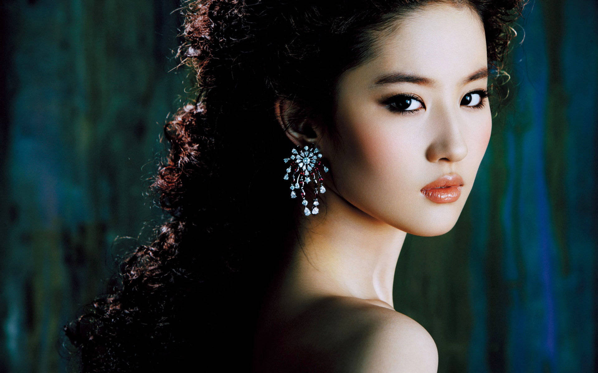Actress 桌布 壁紙 — 一位擁有深色捲髮和閃亮耳環的迷人女性，在憂鬱的藍綠色背景下溫柔凝視。