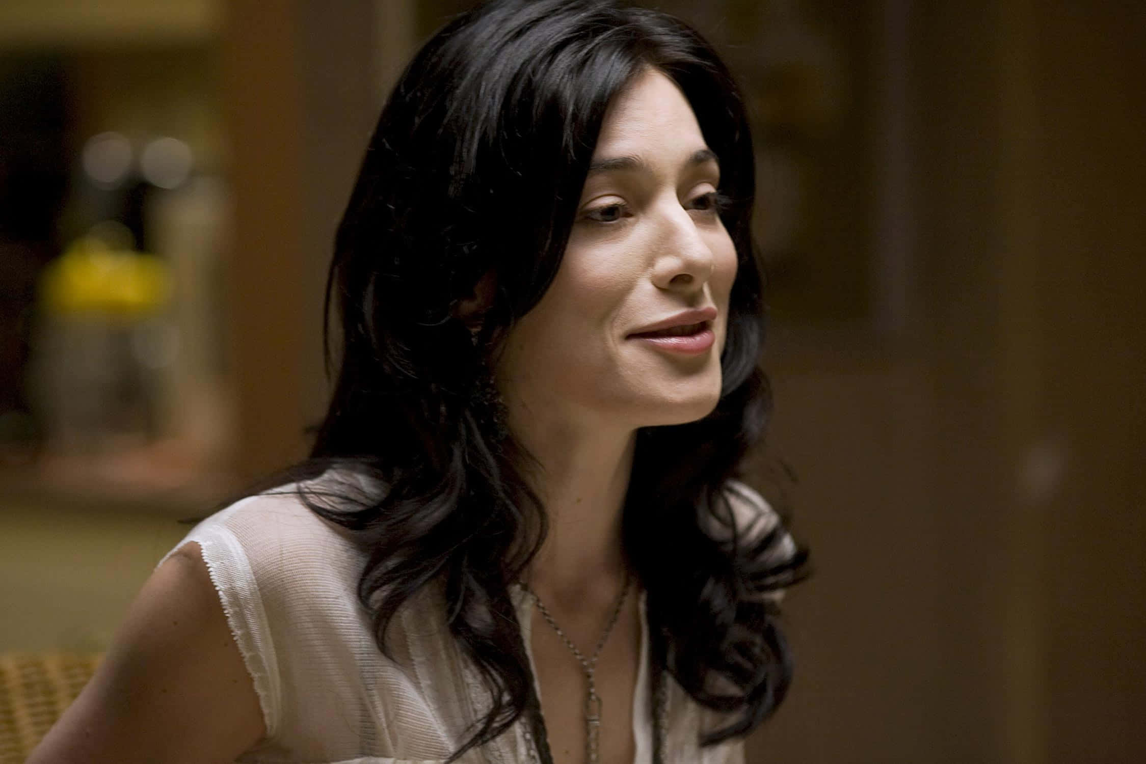 Jaime Murray 桌布 壁紙 — 一位擁有深色波浪長髮的女性在溫暖的室內環境中微笑著，視線離開鏡頭。