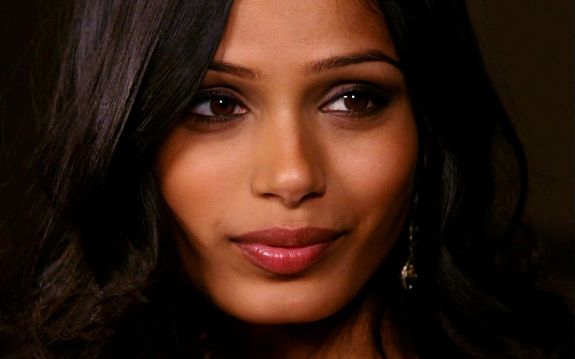 Freida Pinto 桌布 壁紙 — 一位擁有深色波浪髮和溫暖棕色眼睛的女性特寫肖像，溫柔地凝視著觀看者。
