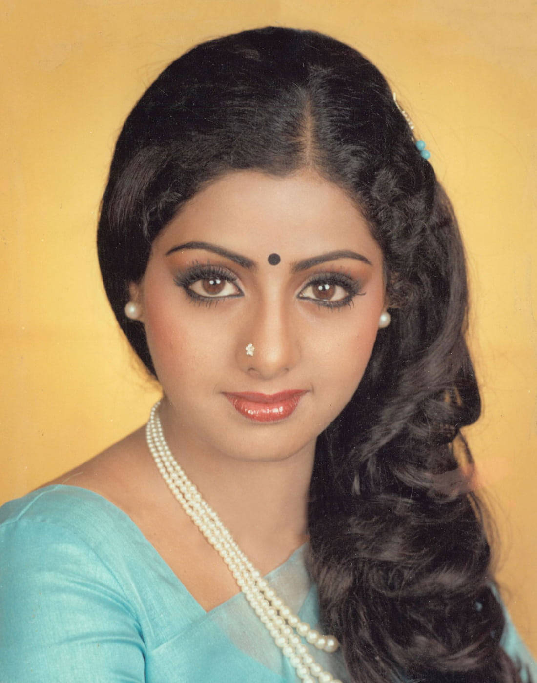 Sridevi 桌布 壁紙 — 一位擁有深色波浪髮和珍珠首飾的女性，在溫暖的黃色背景下穿著藍綠色紗麗。