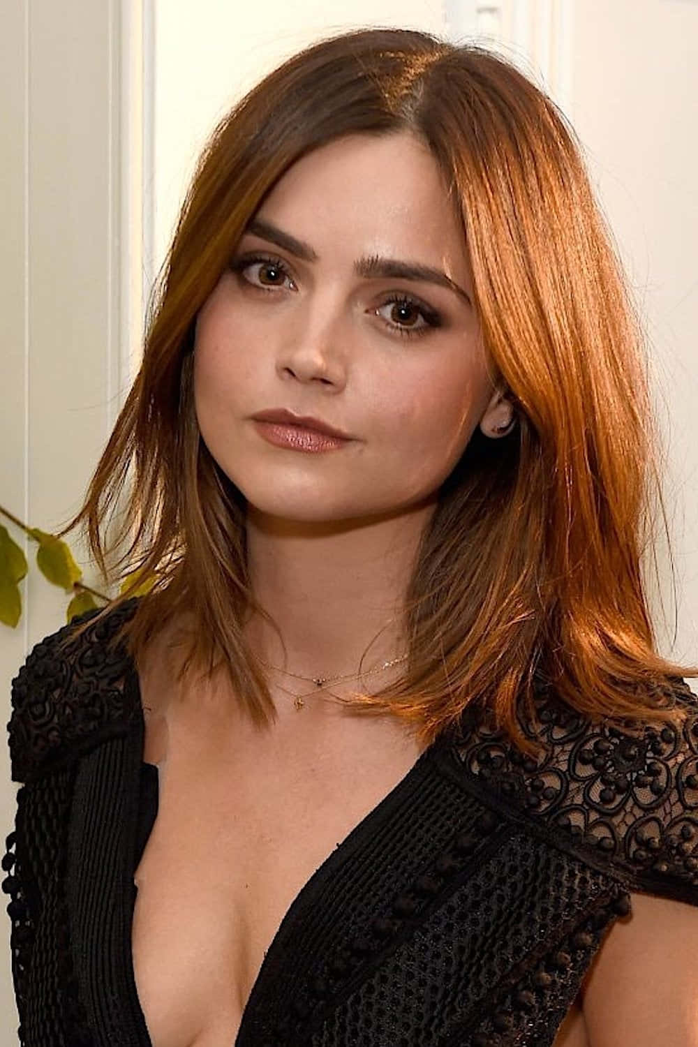 Jenna Coleman 桌布 壁紙 — 一位擁有溫暖棕色頭髮和深色眼睛的女性，在淺色背景下穿著黑色蕾絲上衣，溫柔地凝視著。