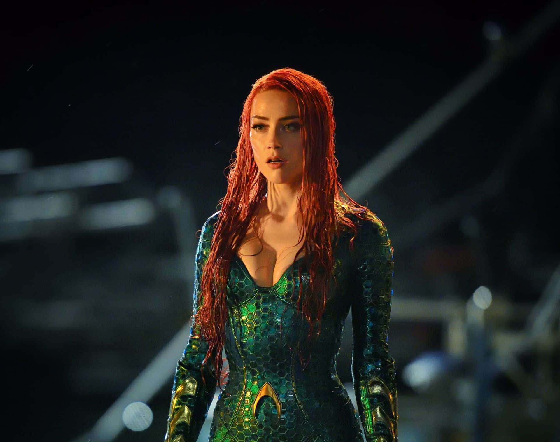 Amber Heard 桌布 壁紙 — 一位擁有濕漉漉紅髮、身穿綠色鱗片狀服裝的女性，站在昏暗光線中，背後是模糊的工業建築。