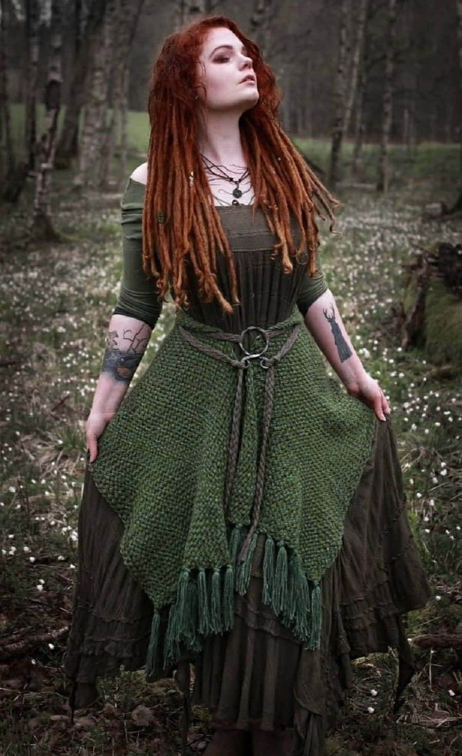 Witch Costumes 桌布 壁紙 — 一位擁有火紅辮子的女性站在迷霧森林中，身穿帶流蘇的土綠色分層連衣裙，手臂上可見紋身。