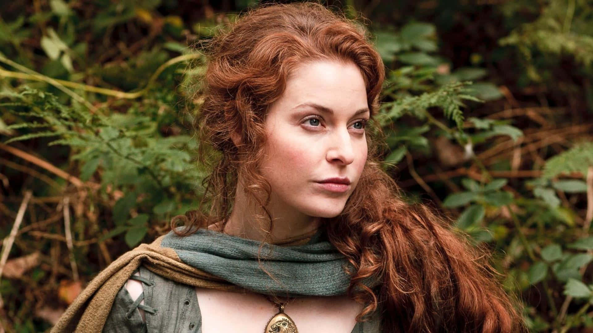 Esmé Bianco 桌布 壁紙 — 一位擁有火紅頭髮和綠色圍巾的女性，若有所思地凝視著一片蕨類植物茂密的森林。