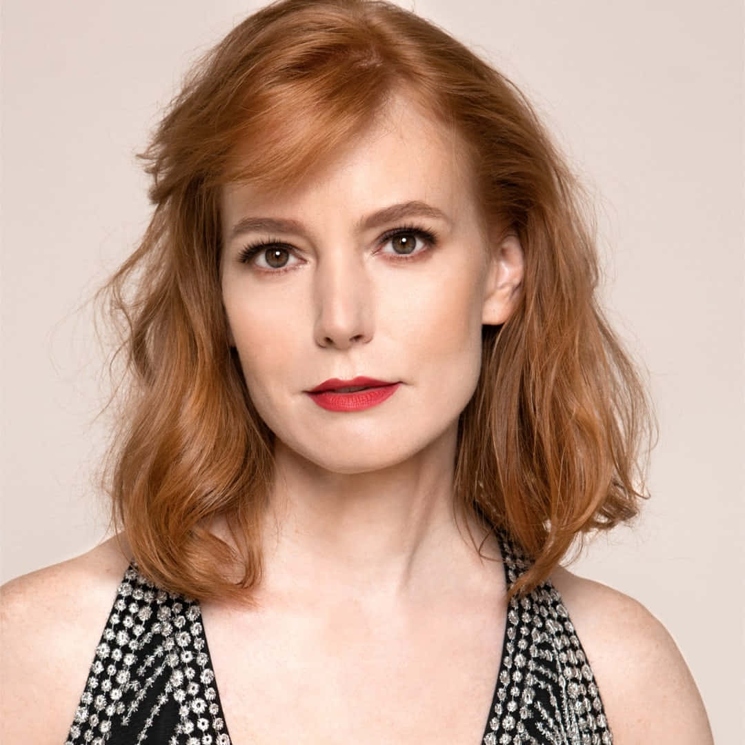 Alicia Witt 桌布 壁紙 — 一位擁有火紅頭髮和鮮豔紅唇的女性，在柔和的米色背景下直視鏡頭。