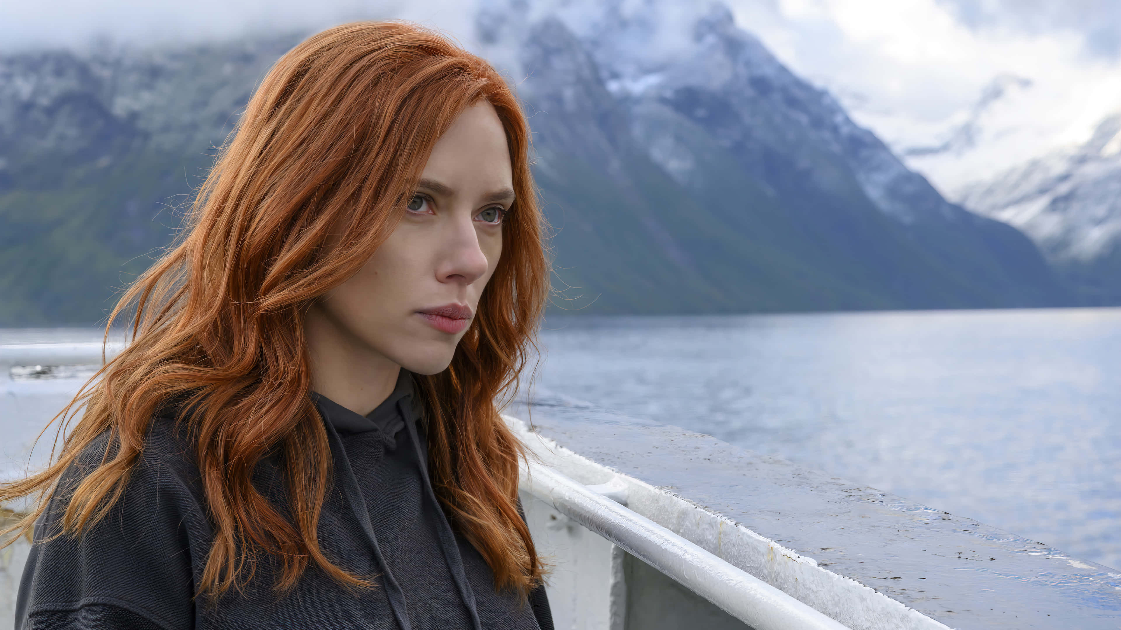 Natasha Romanoff 桌布 壁紙 — 一位擁有火紅頭髮的女性站在船欄杆上，在陰天中若有所思地凝視著霧氣繚繞的山間湖泊。