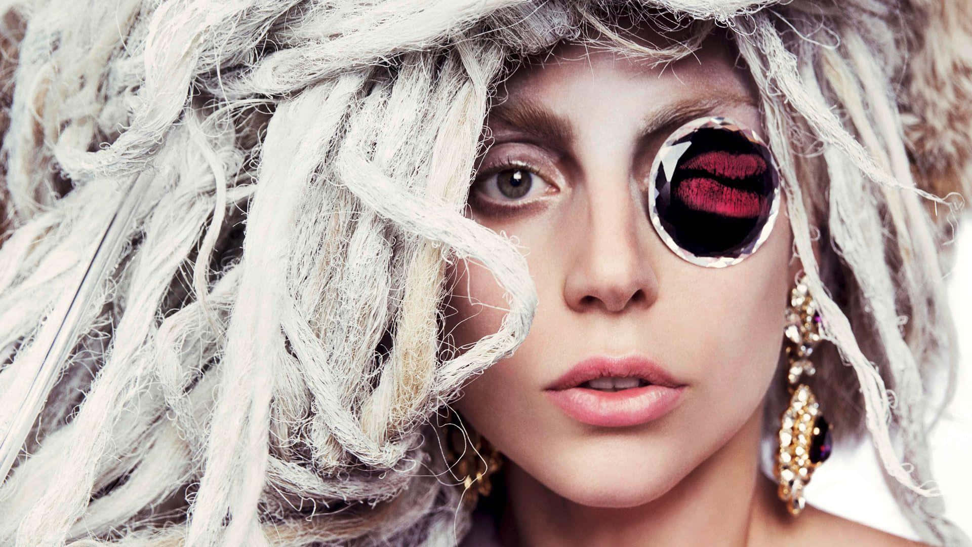 Lady Gaga 桌布 壁紙 — 一位擁有狂野白髮的女性戴著單片眼鏡，在純白背景上反射出紅唇和華麗的金耳環。