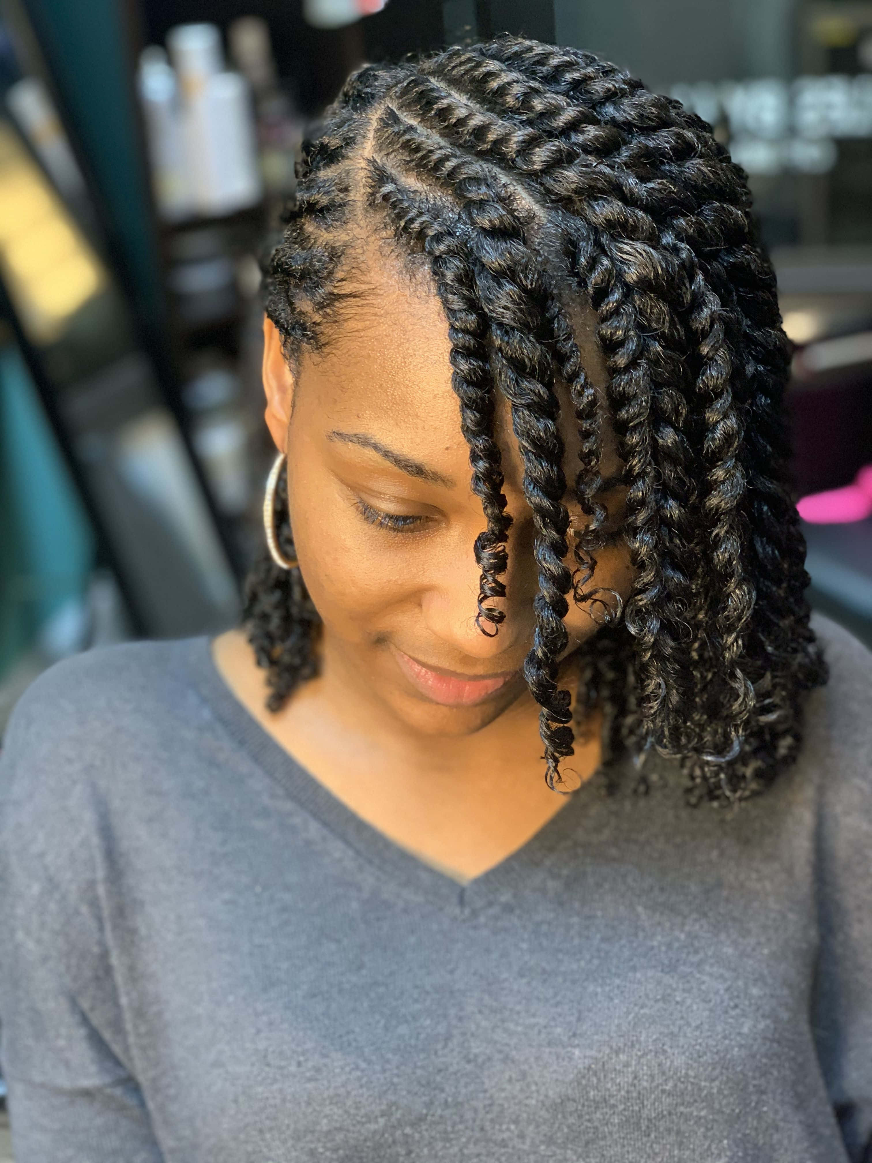 hair 桌布 壁紙 — 一位擁有精緻箱形辮子和溫柔微笑的女性在沙龍環境中低頭。