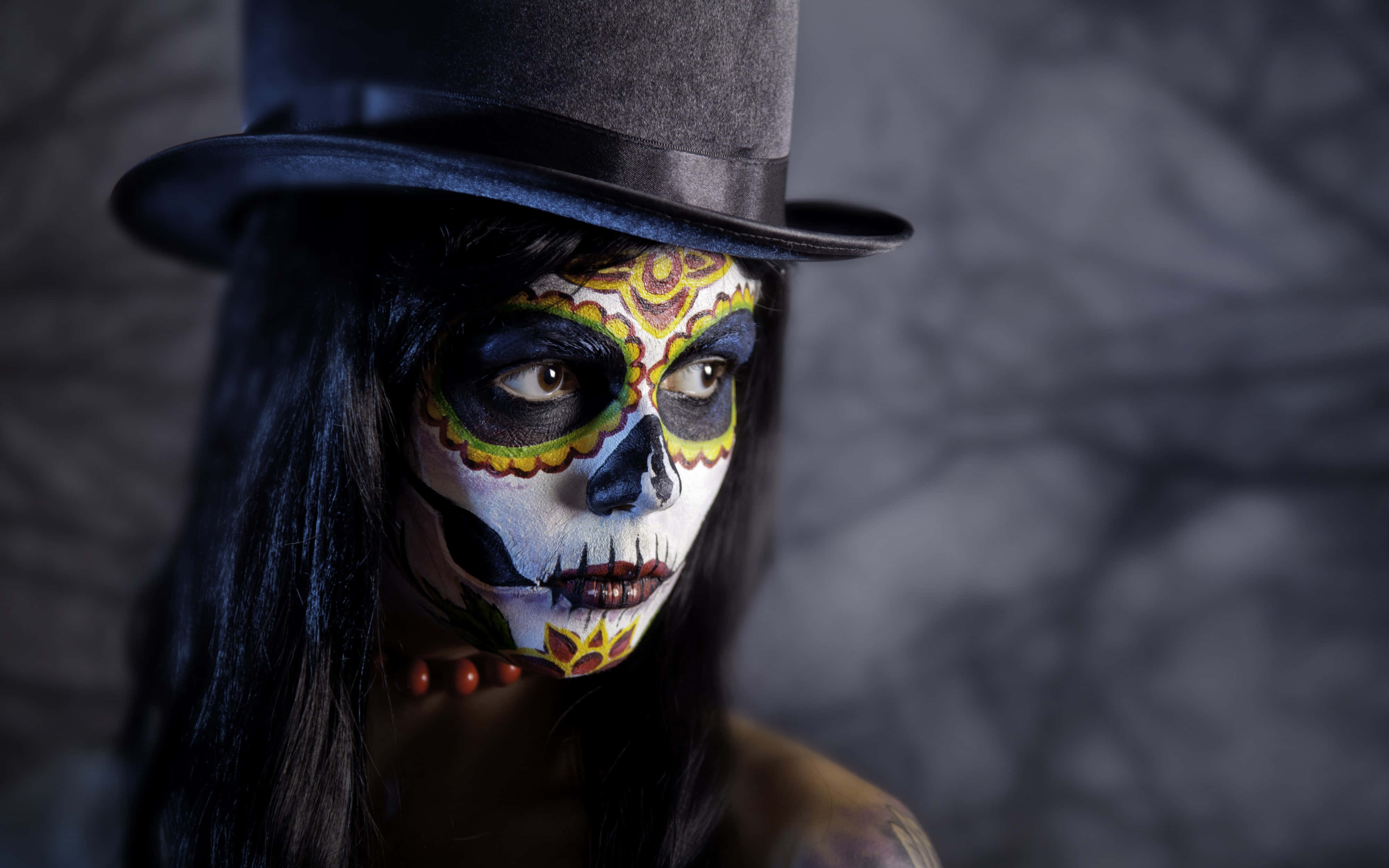 Halloween Tattoos 桌布 壁紙 — 一位擁有精緻糖骷髏妝容和黑色高頂帽的女性，在深色紋理背景前凝視著。
