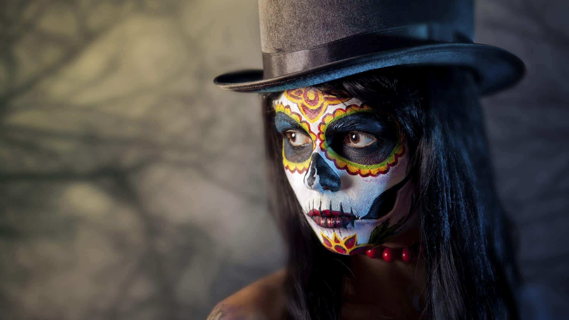 亡靈節 桌布 壁紙 — 一位擁有精緻糖骷髏妝容和黑色高頂帽的女性，在模糊的石頭背景下凝視著。
