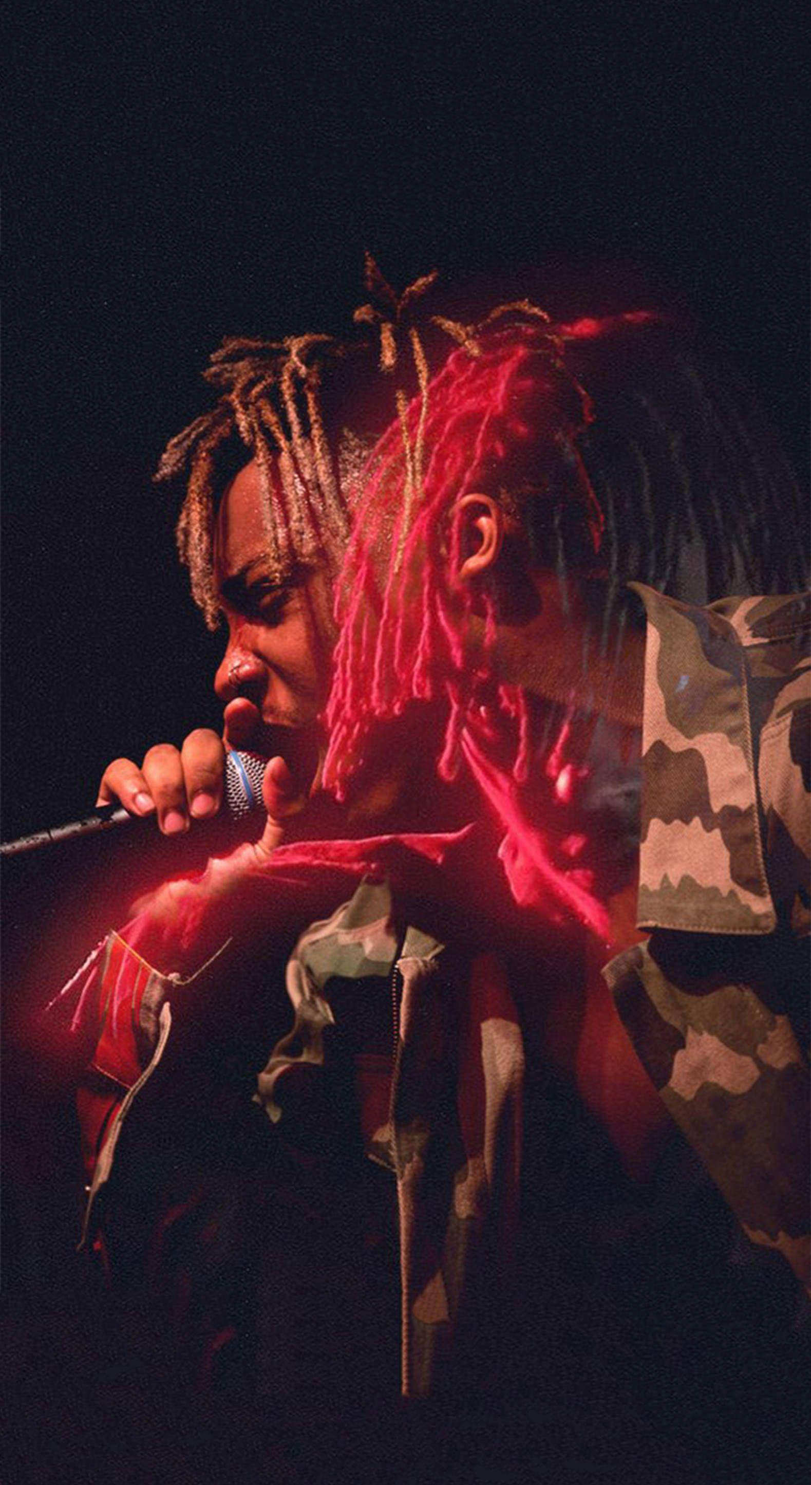 Juice WRLD 桌布 壁紙 — 一位擁有紅色發光辮子的音樂家在昏暗的舞台燈光下，穿著迷彩外套對著麥克風唱歌。
