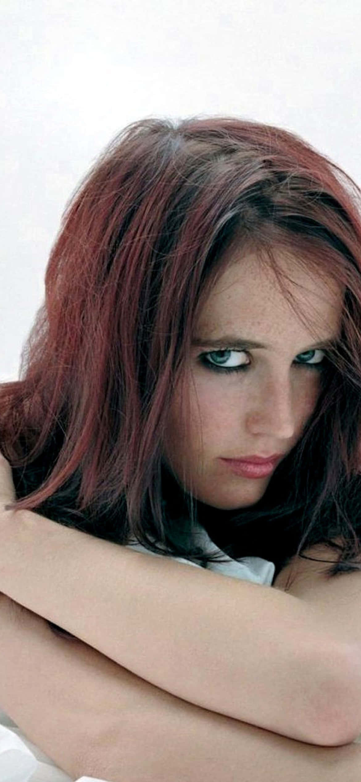 eva green 桌布 壁紙 — 一位擁有紅褐色頭髮和強烈綠色眼睛的女性，在純白色背景前交叉雙臂，直視鏡頭。