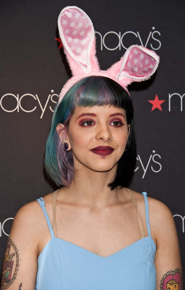 Melanie Martinez 桌布 壁紙 — 一位擁有藍綠色頭髮和兔耳朵的女性在梅西百貨活動中穿著淺藍色上衣擺姿勢。