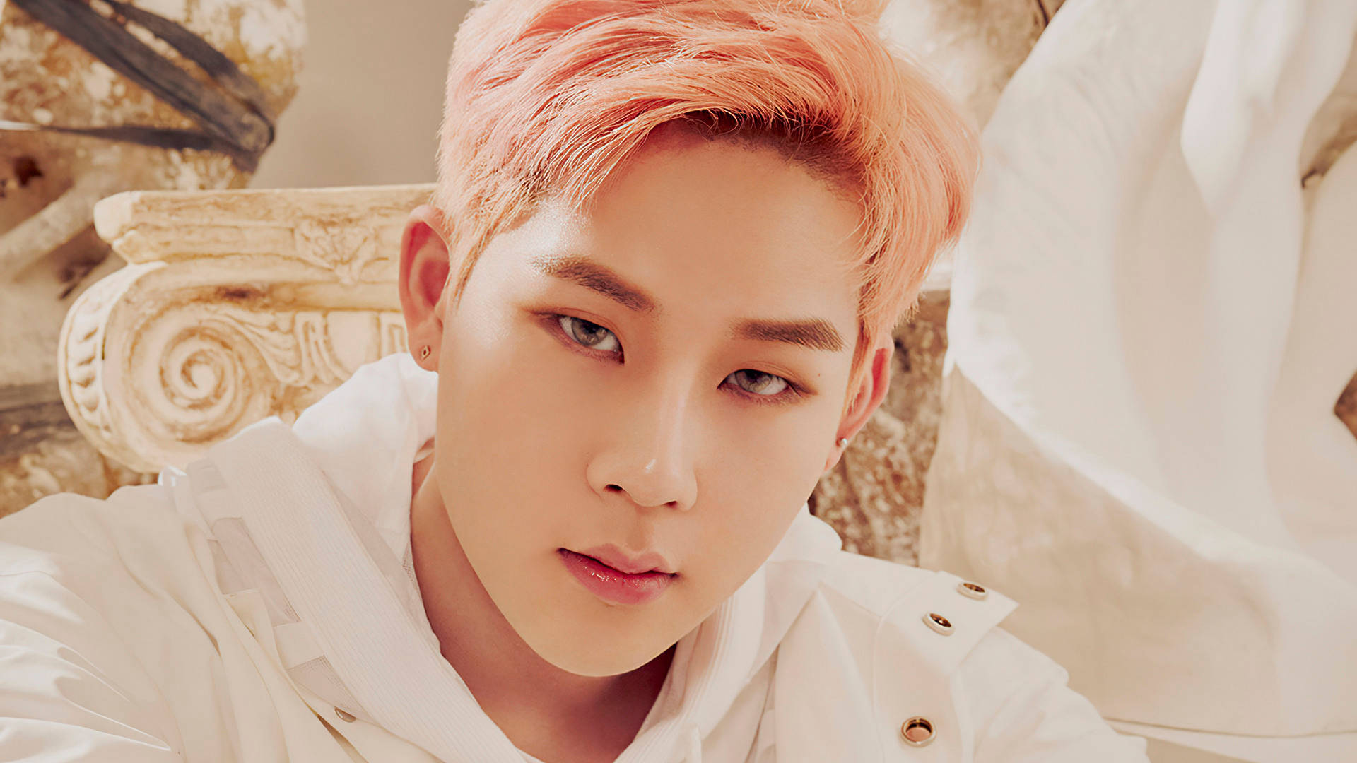 Monsta X Jooheon Fantasia X 壁紙 — 一位擁有蜜桃色頭髮和銳利眼神的年輕男子，坐在華麗的白色椅子上，凝視著前方。
