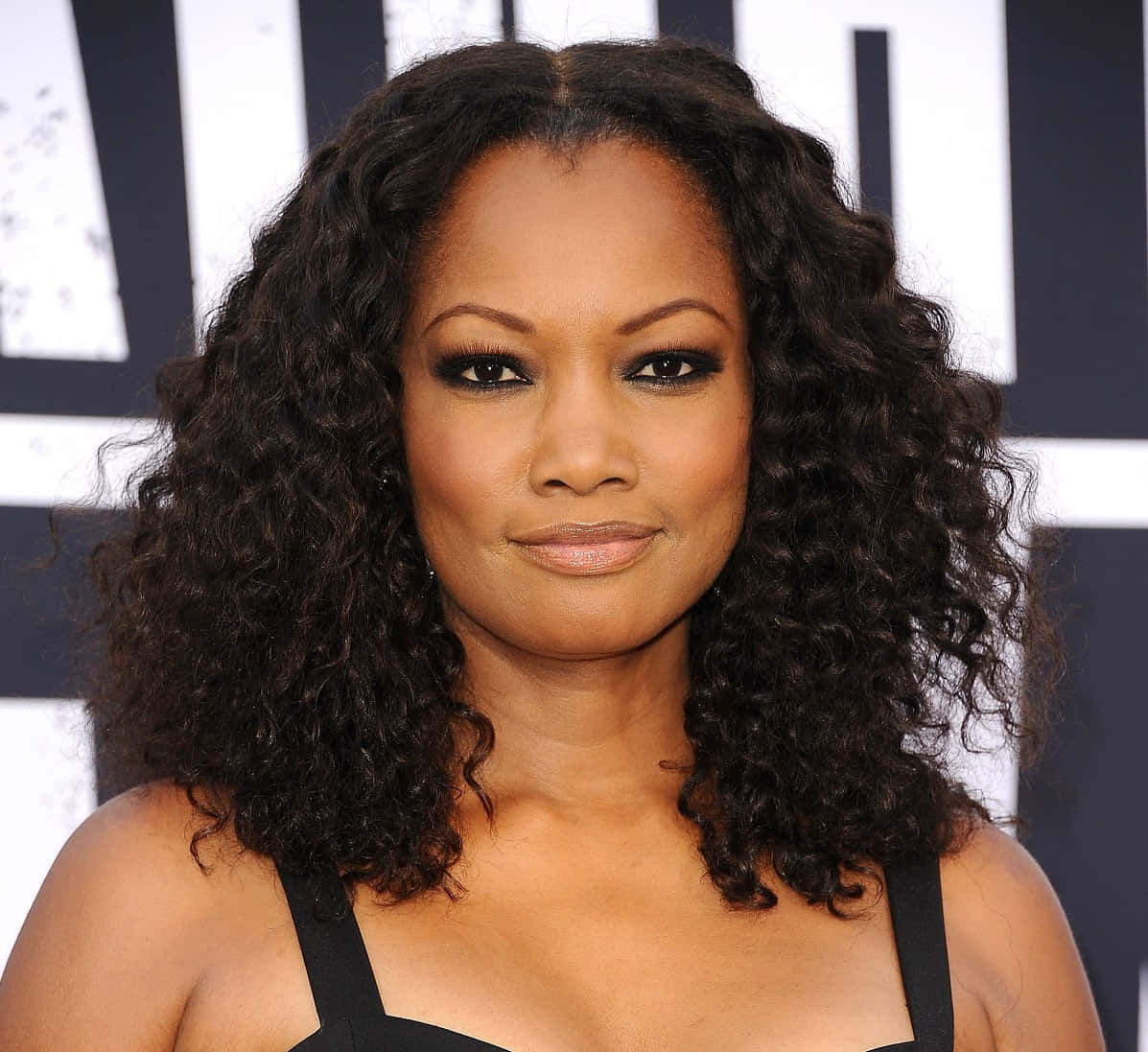 Garcelle Beauvais 桌布 壁紙 — 一位擁有豐盈深色捲髮和大膽妝容的女性，在黑白條紋背景前自信地擺姿勢。