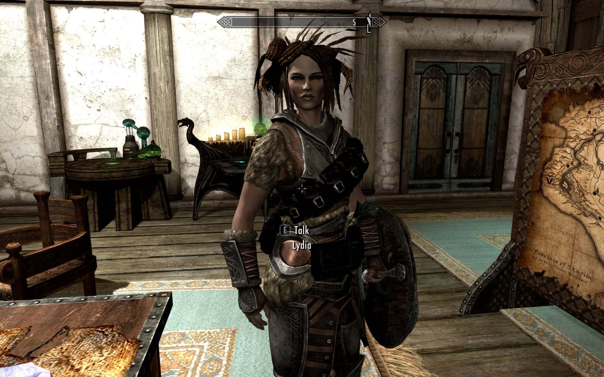 Skyrim Lydia 桌布 壁紙 — 一位擁有辮子頭和盔甲的女戰士站在一個有木製家具和大地圖的質樸石室中。