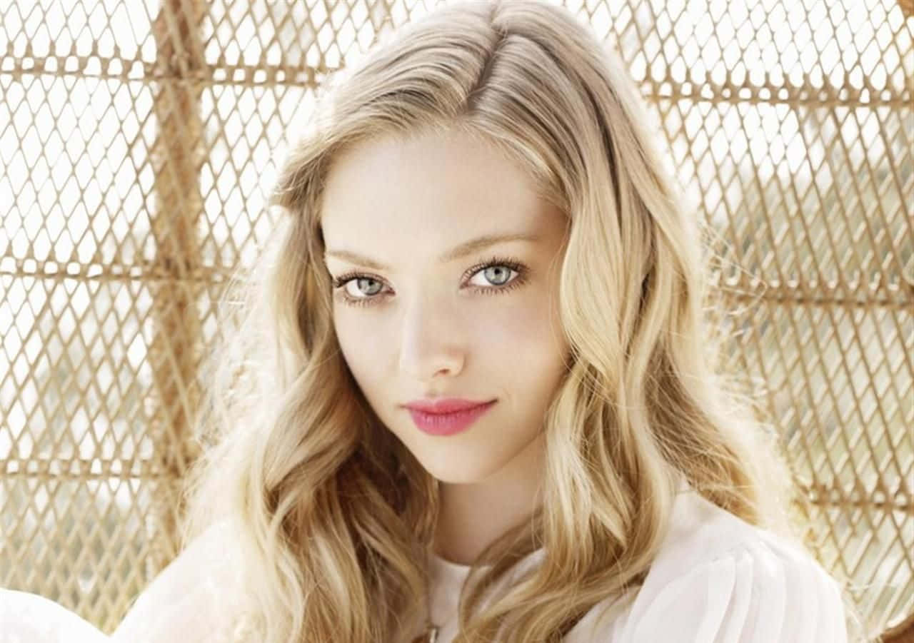 Amanda Seyfried 桌布 壁紙 — 一位擁有金色長髮和藍色眼睛的女性，在編織竹背景前溫柔地凝視。
