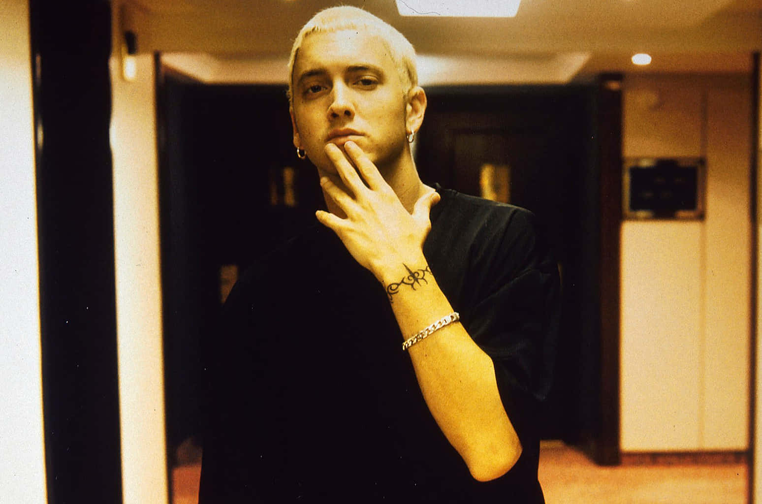 Eminem 桌布 壁紙 — 一位擁有鉑金色頭髮和紋身的男士，在溫暖照明的室內走廊中若有所思地擺姿勢。
